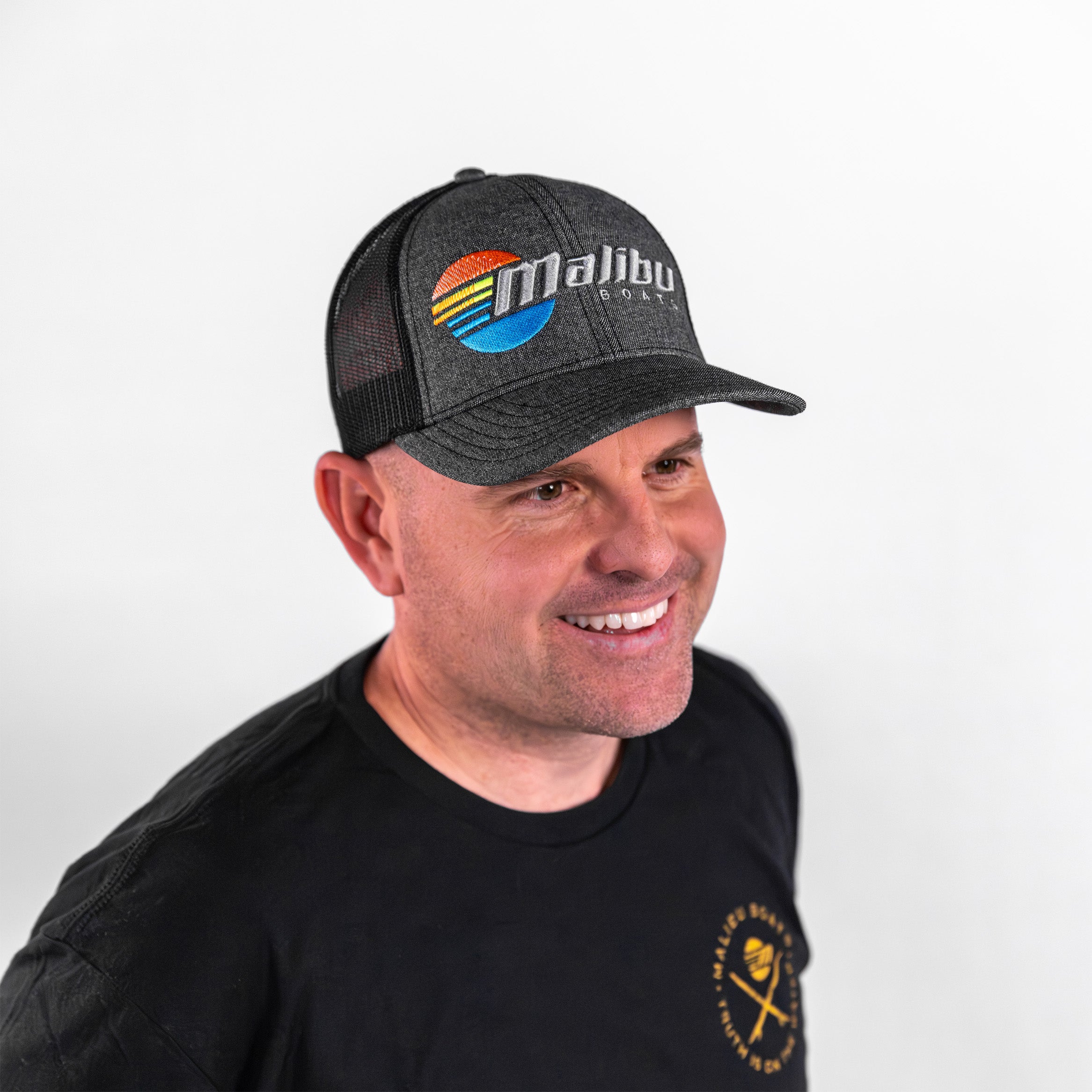 Man wearing a Malibu Trucker Hat with a logo, smiling against a white background. Perfect for boating enthusiasts.