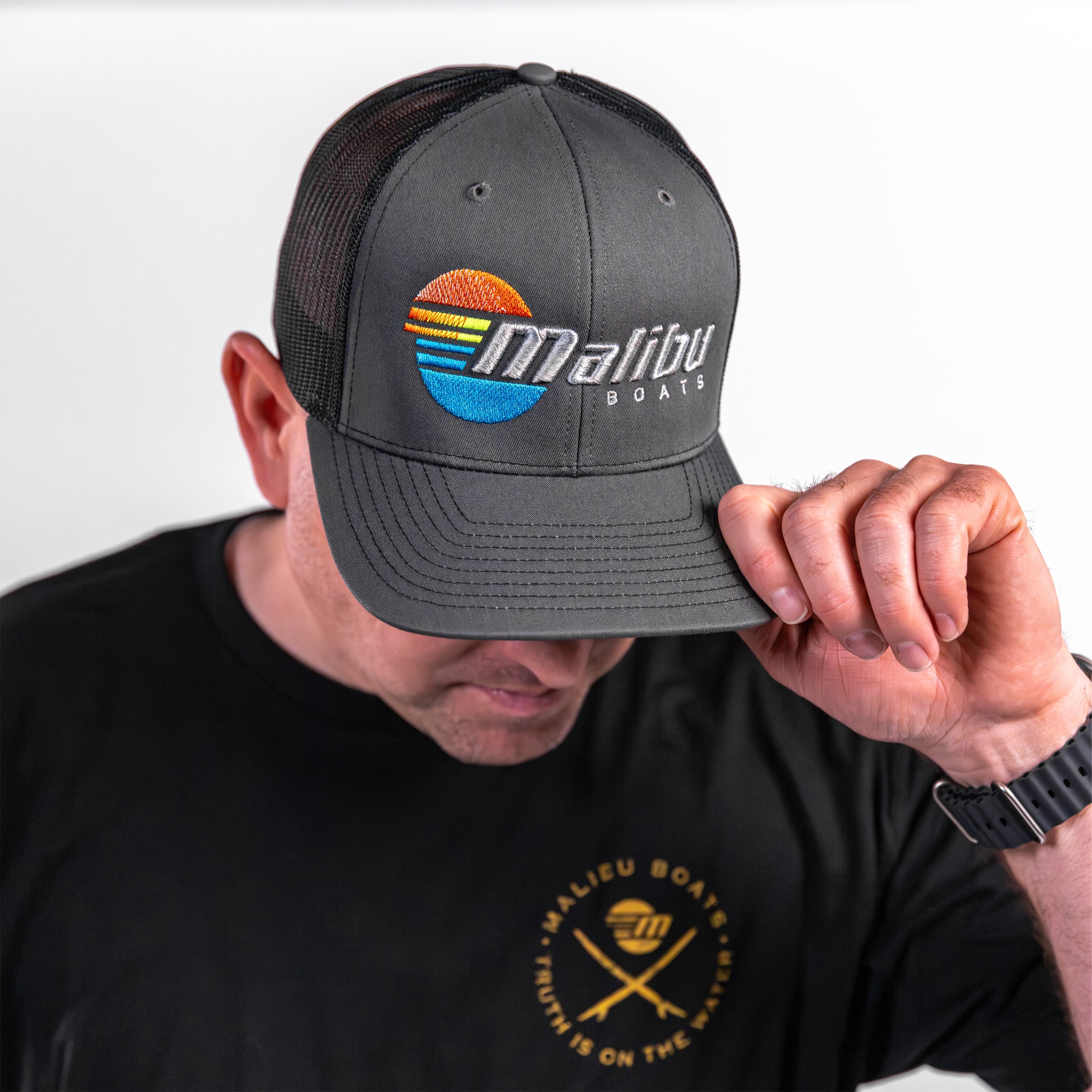 Malibu Trucker Hat featuring a colorful logo, worn by a person in a black Malibu Boats t-shirt.