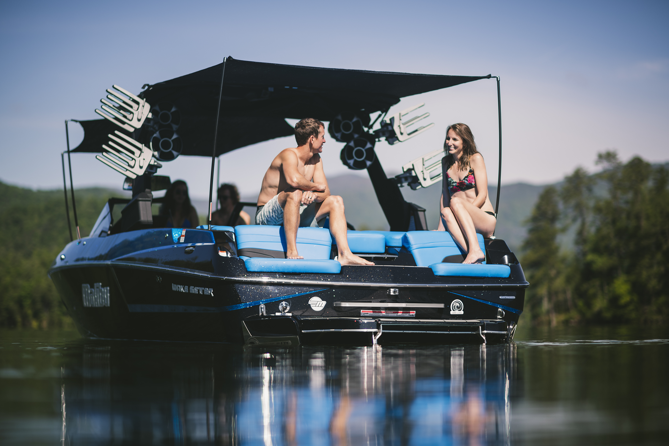 People relaxing on a Malibu 24MXZ Solo Mesh Awning G3 Tower boat with a 20-foot canopy, enjoying a day on the water.