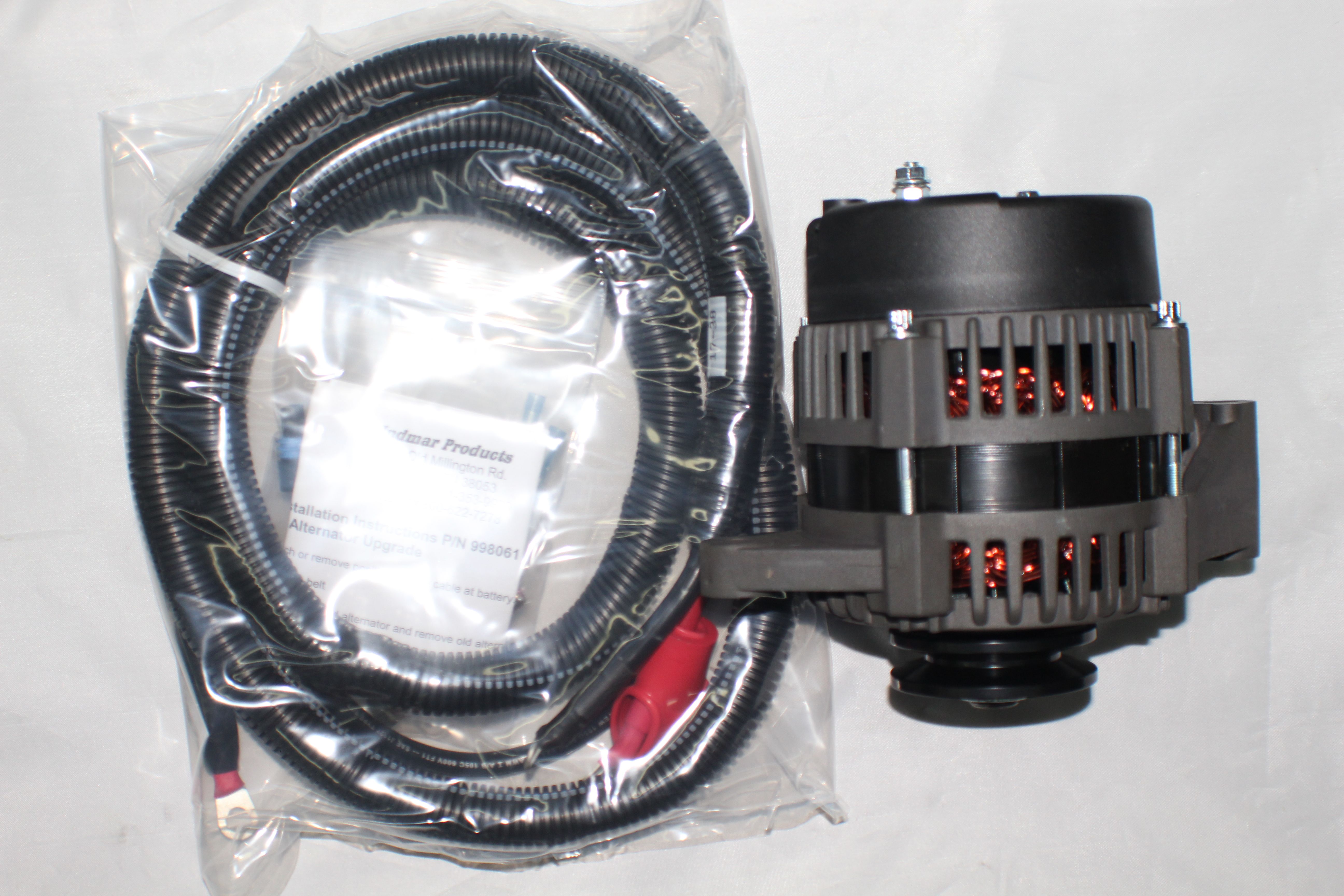 Indmar 70 AMP alternator kit with a black and gray alternator and a coiled wiring harness in clear plastic packaging.