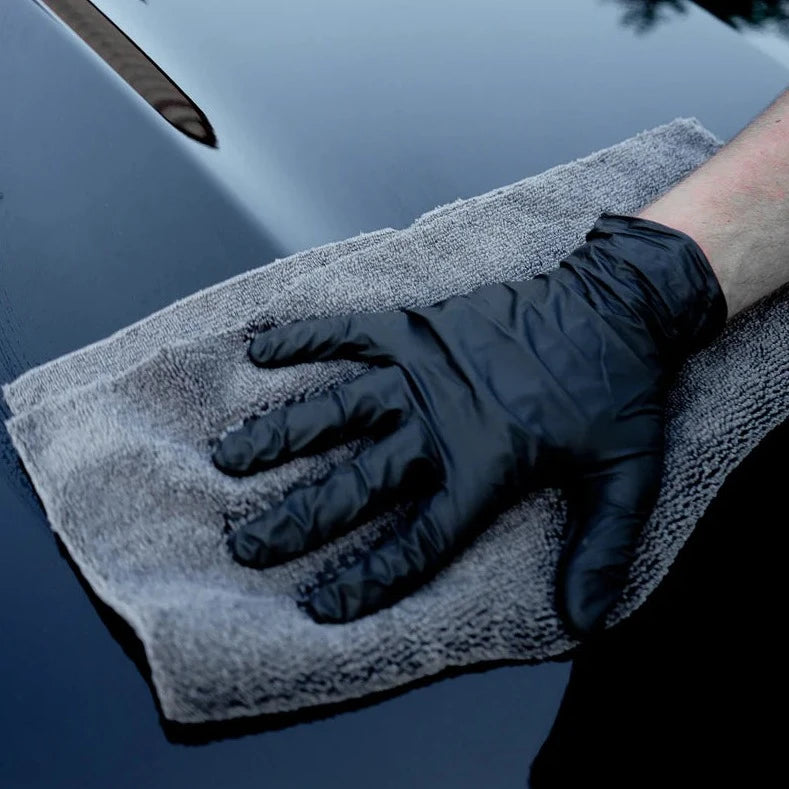 Two microfiber towels in a 2-pack, with one being used to wipe a car surface, featuring edgeless design for scratch-free cleaning.