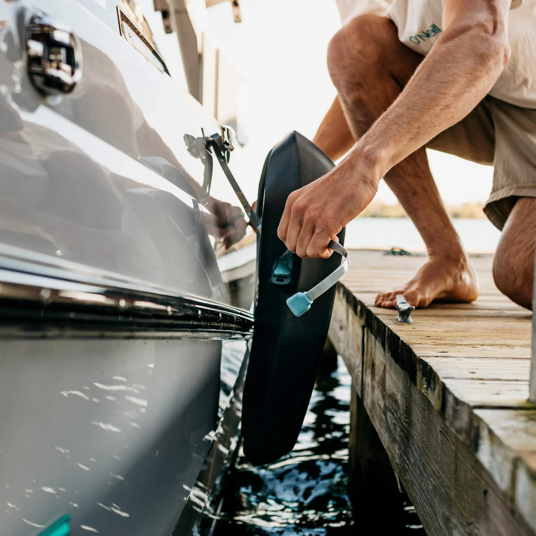 A person attaching a Mission Boat SENTRY 2.0 boat fender to a boat docked at a marina, with water in the background.