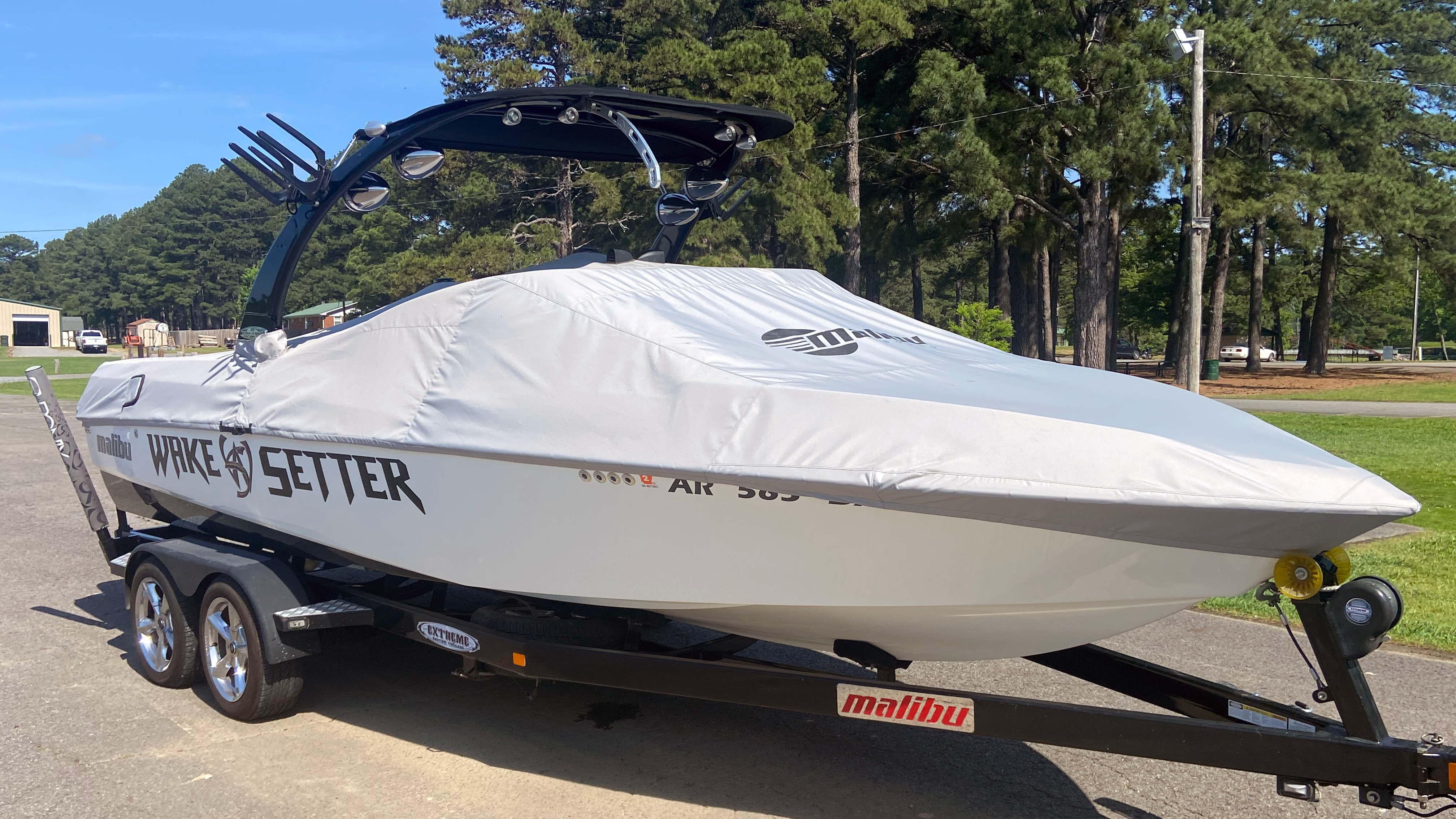 Sunscape/Wakesetter 247 boat cover with Illusion X/XS Tower, 63" height, on a trailer outdoors with trees in the background.