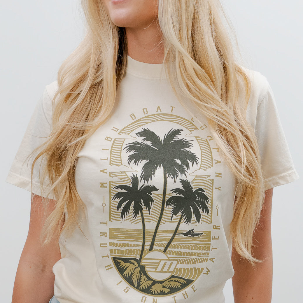 Cream-colored Malibu Beach Tee featuring a graphic of palm trees, ocean, and surf, perfect for casual beachwear.