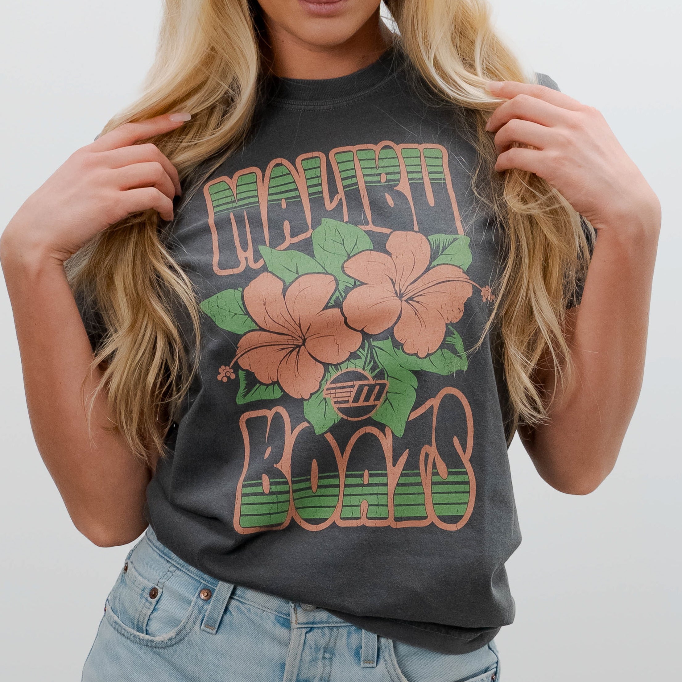 Black Malibu Aloha T-shirt with pink hibiscus flowers and green "Malibu Beaches" text, worn by a woman with blonde hair.