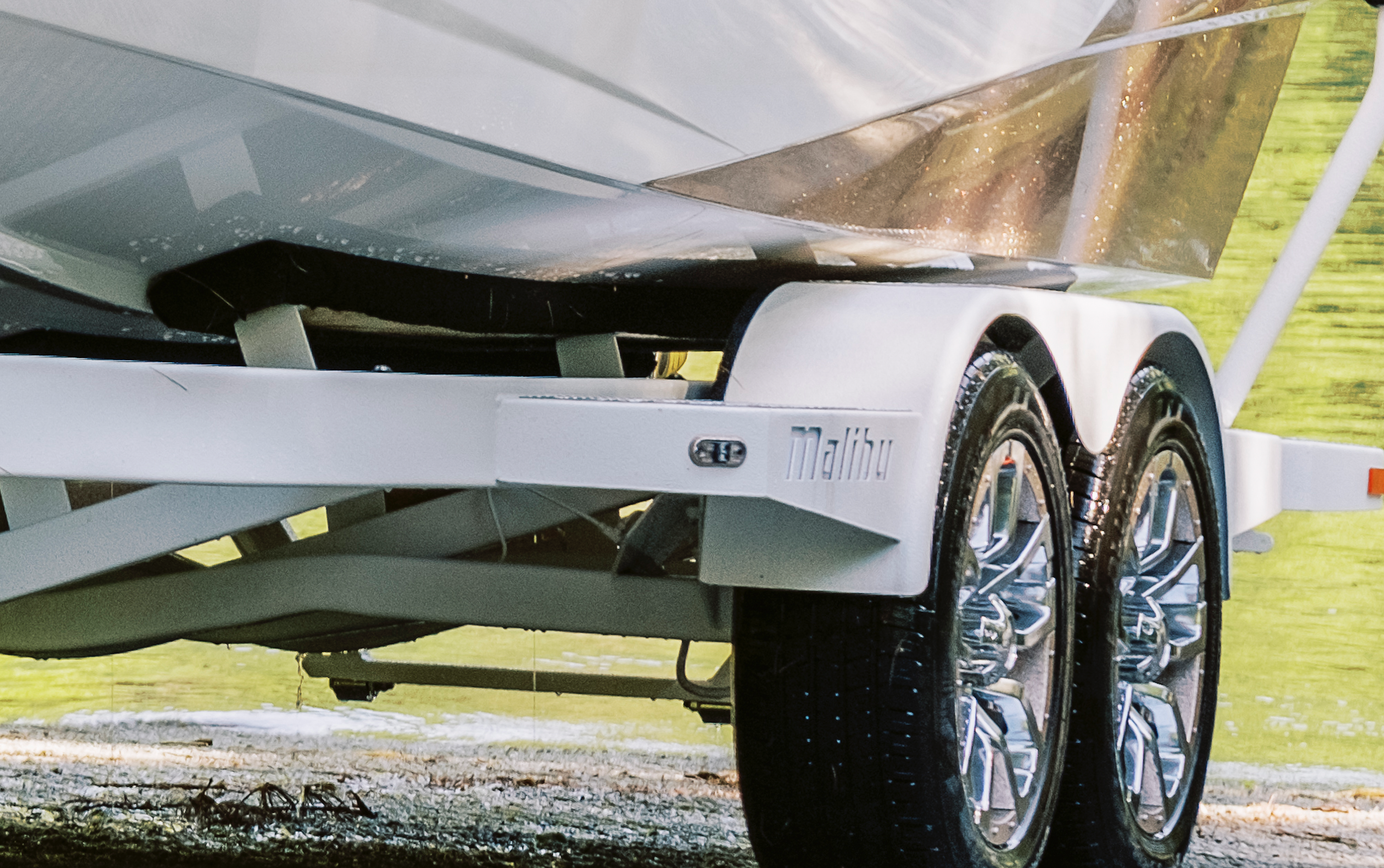 Close-up of a Malibu front trailer step with dual wheels, mounted on a white trailer frame, outdoors on grass.