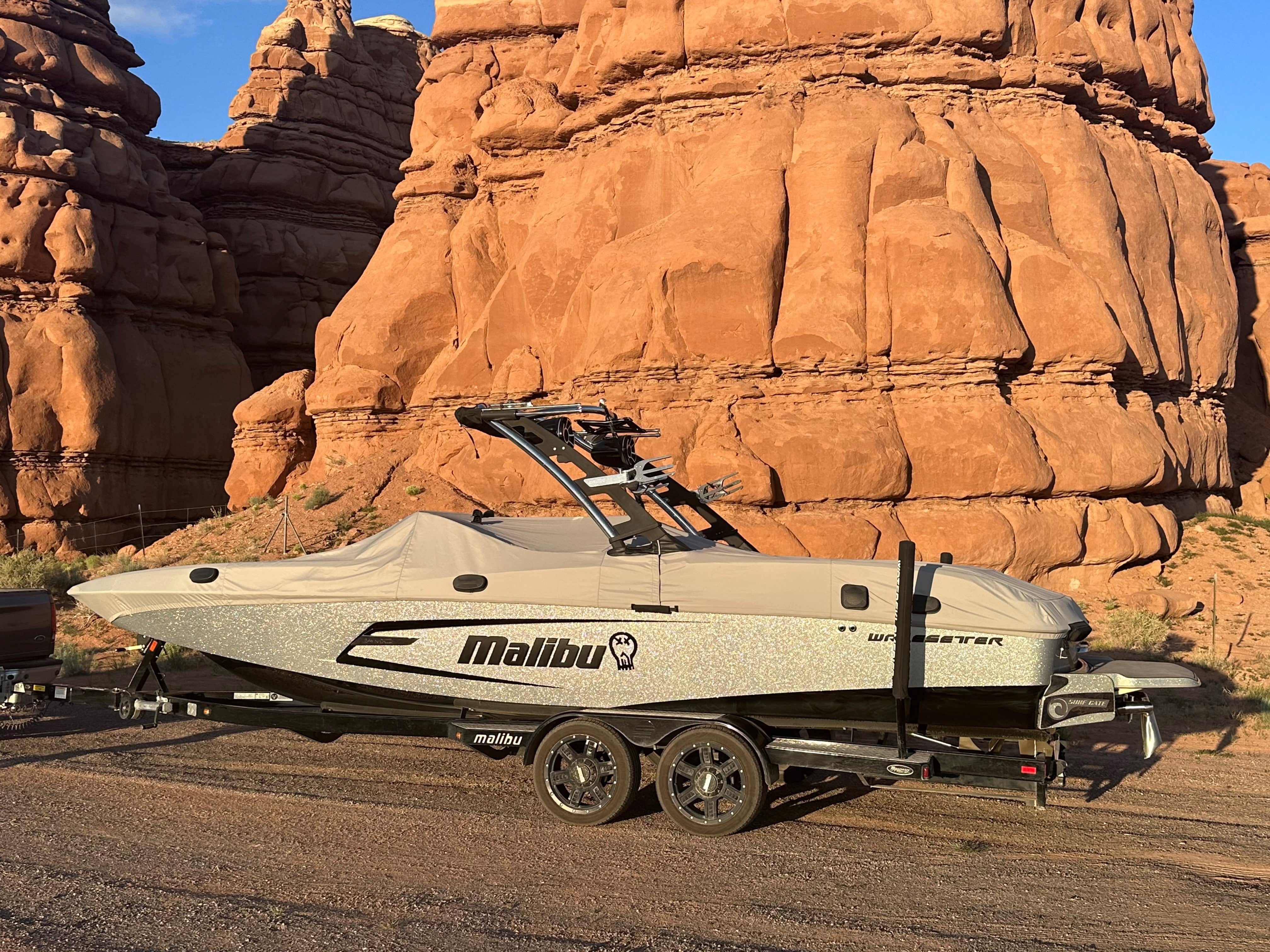 Malibu boat with 24 MXZ G3 Tower cover on trailer, parked near red rock formations in desert landscape.