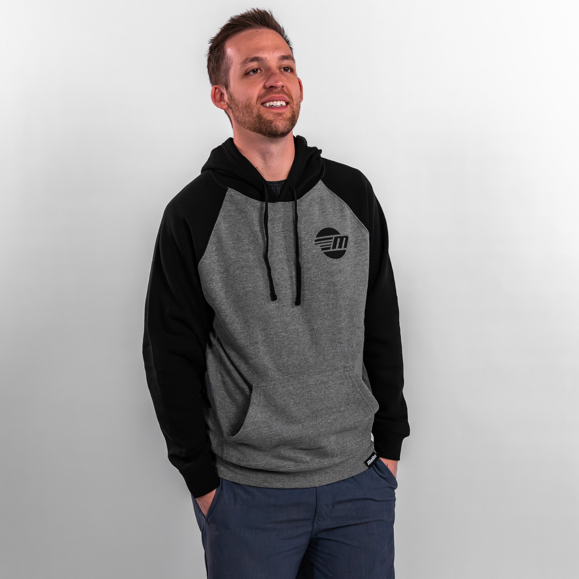 A man wearing a gray and black Malibu hoodie with a logo, smiling against a neutral background.