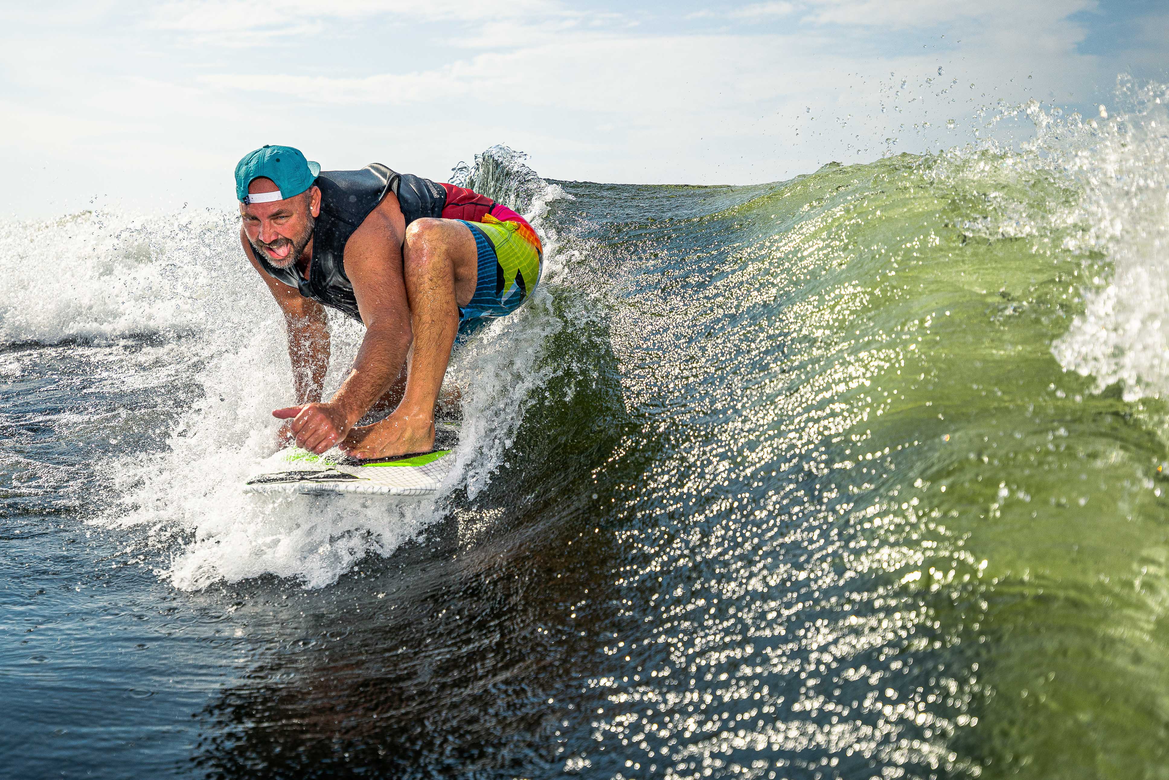 A man surfing on the 2025 Phase 5 Doctor Surf Board, riding a green wave with a focused expression and colorful swimwear.