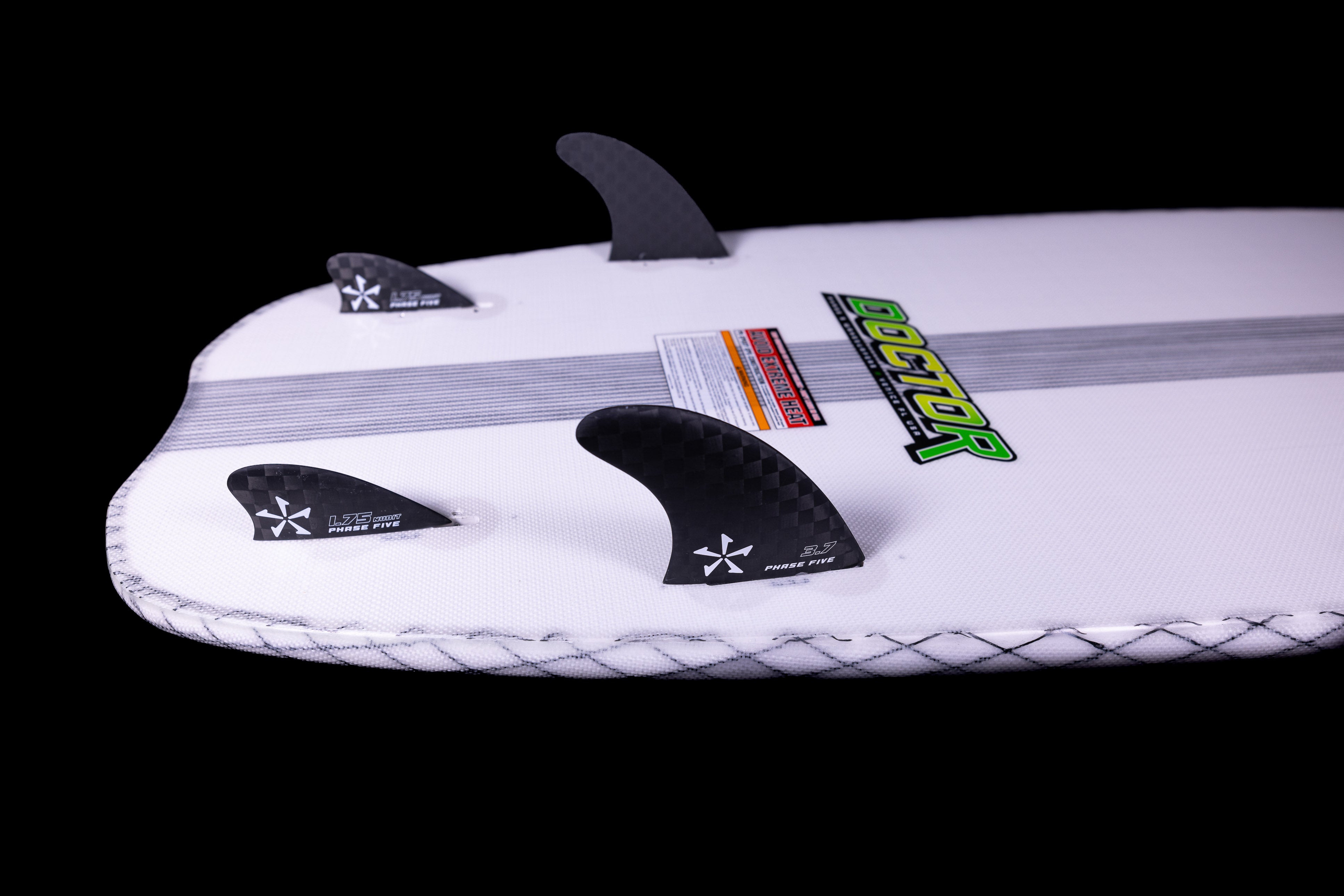 Close-up of a 2025 Phase 5 Doctor surfboard with three black fins, white deck, and colorful branding on a black background.