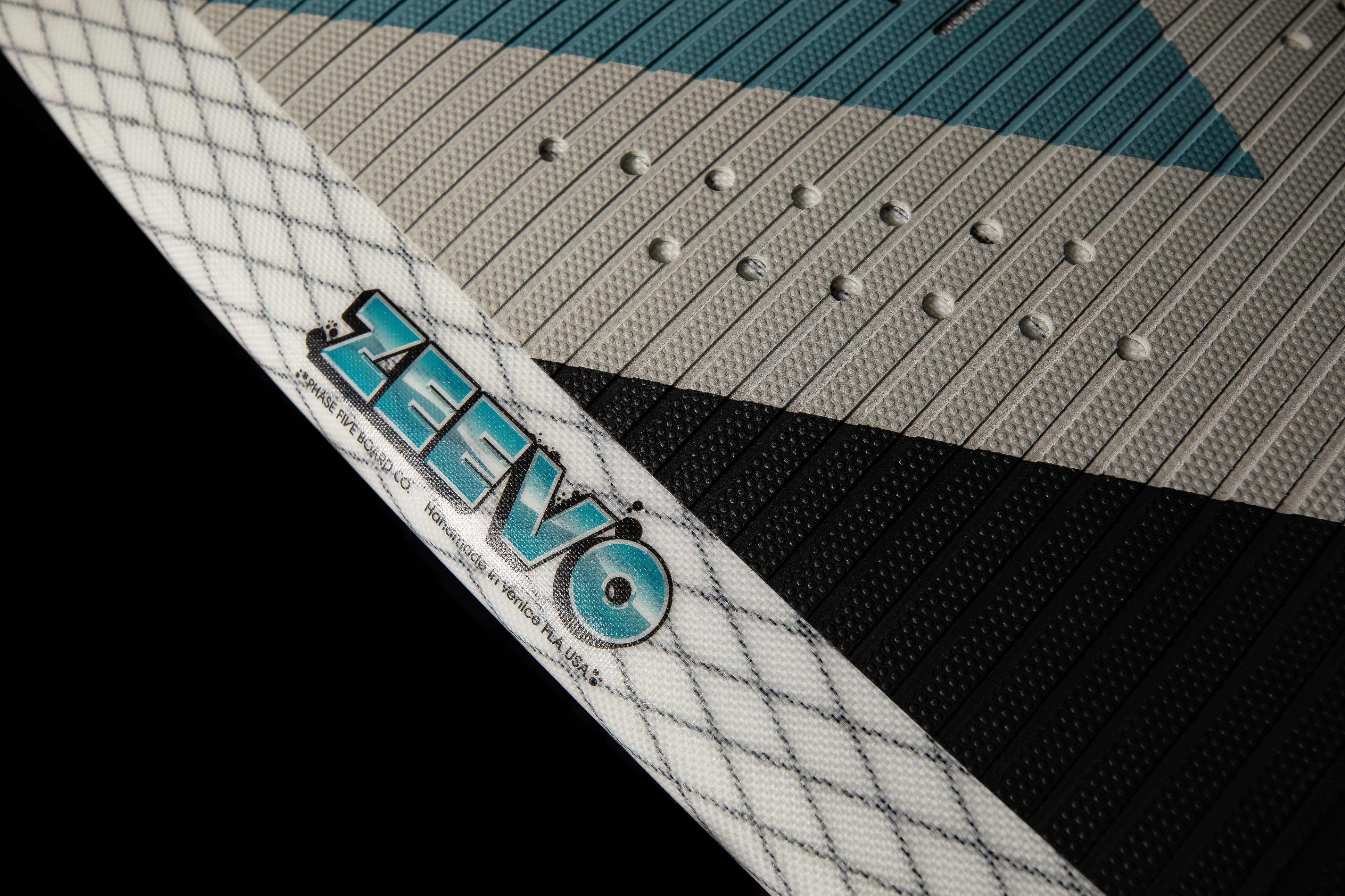 Close-up of the 2025 Phase 5 Zeevo surfboard featuring textured grip pads, a white diamond-patterned edge, and blue branding.