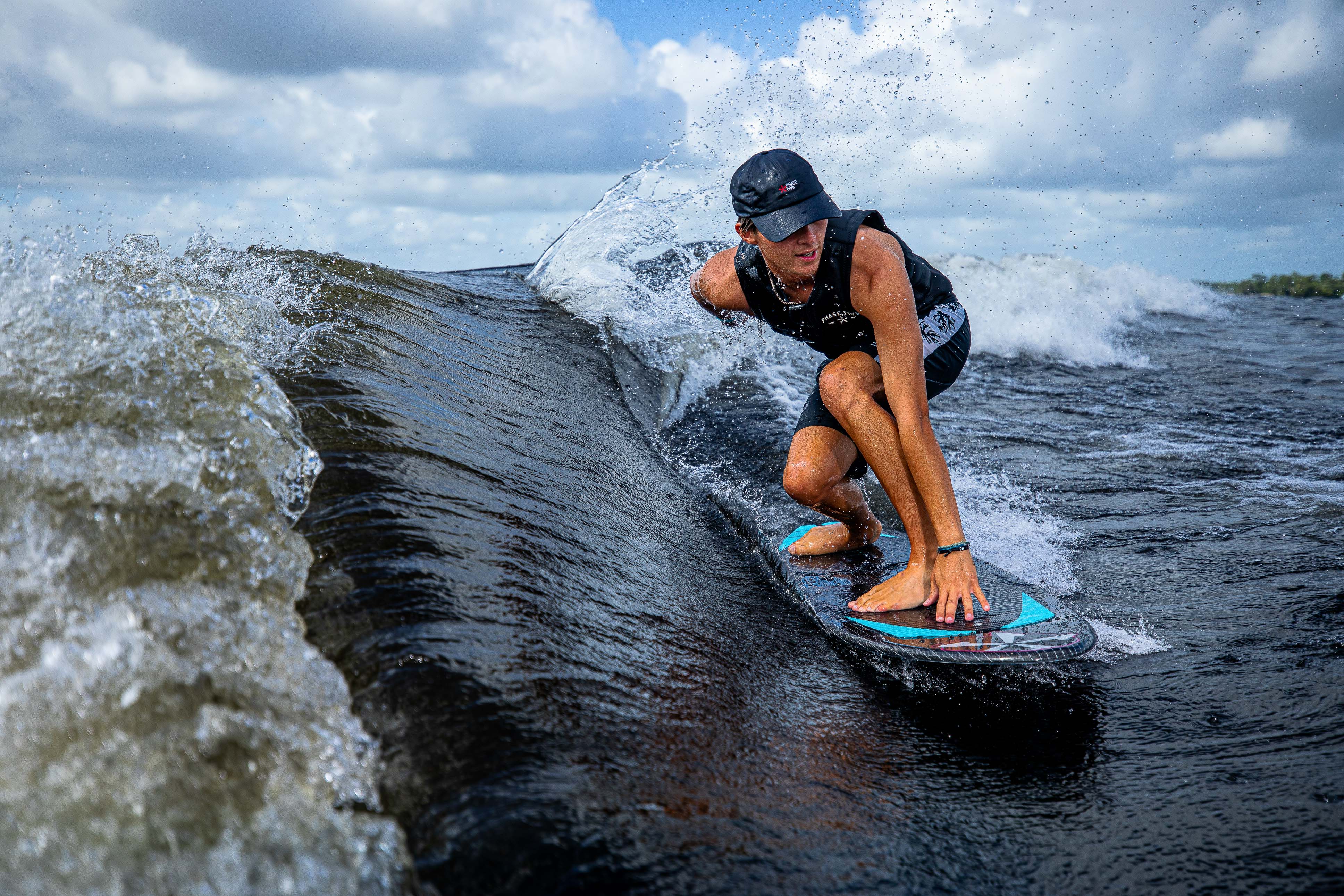 A person rides a 2025 Phase 5 Hypsta skim board on a wave, showcasing dynamic movement and water spray.