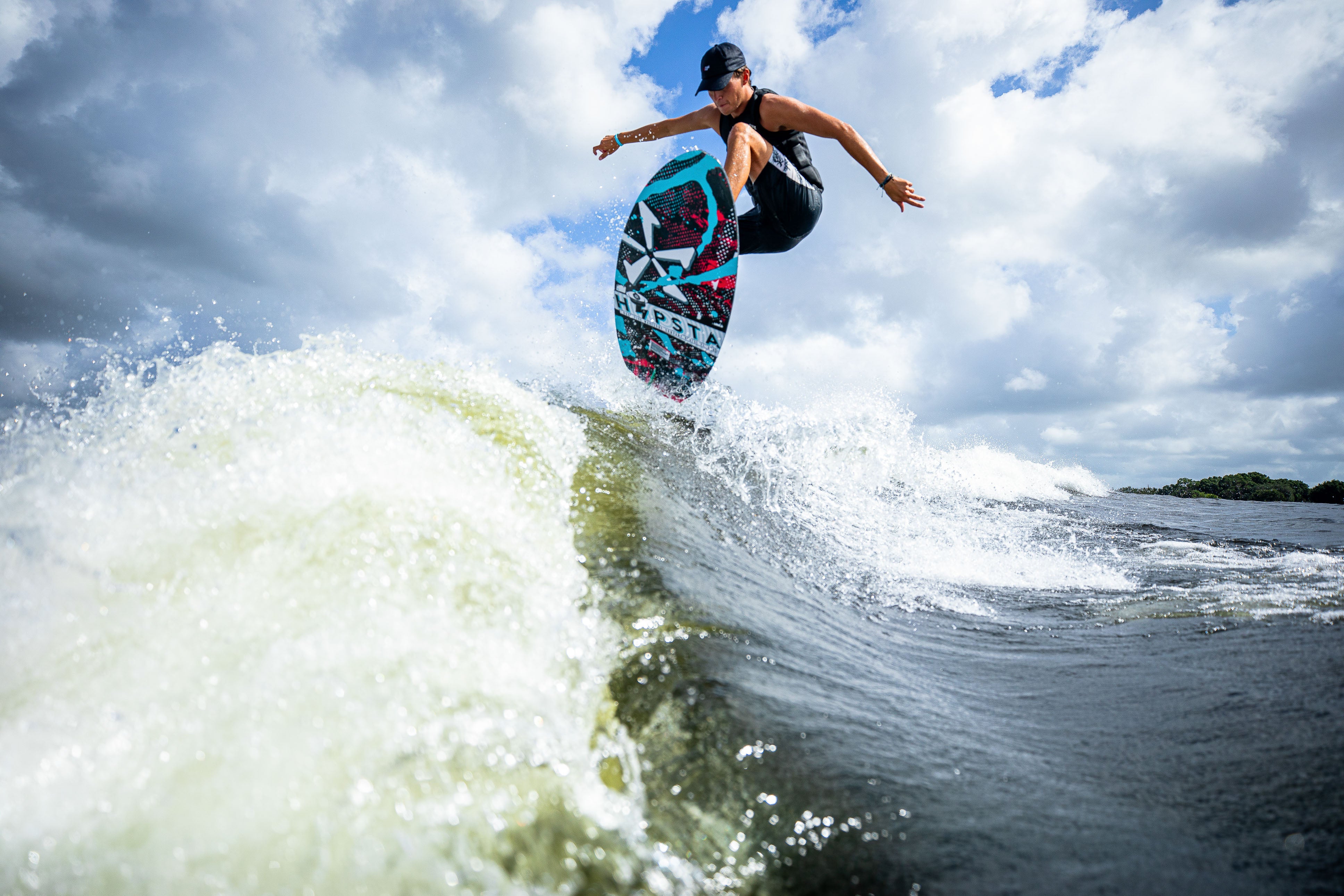 A person performs a jump on a 2025 Phase 5 Hypsta skim board over a wave, showcasing dynamic movement and skill.