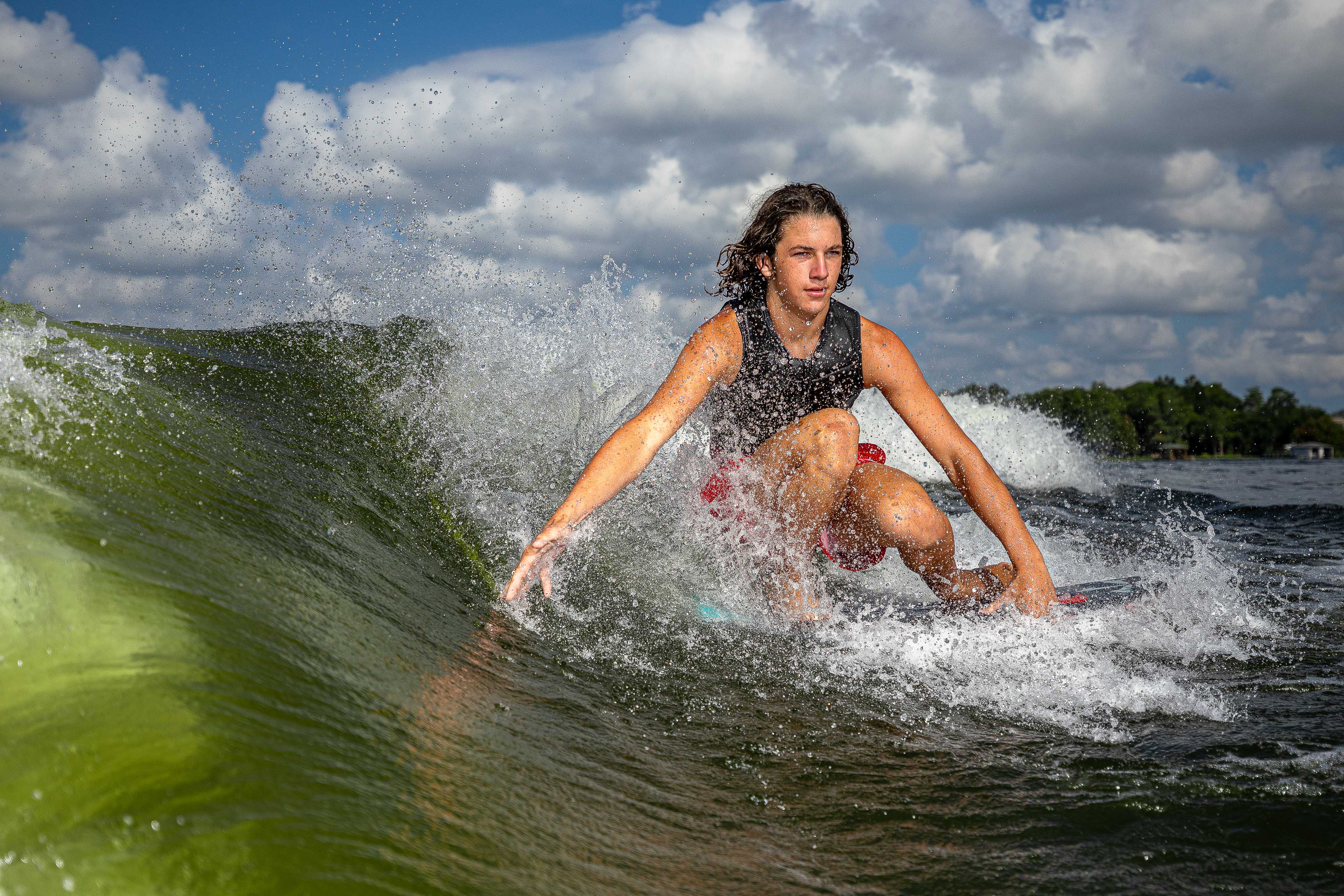 A young man rides a wave on a 2025 Phase 5 Key Jett Shreds skim board, showcasing skill and agility in water.