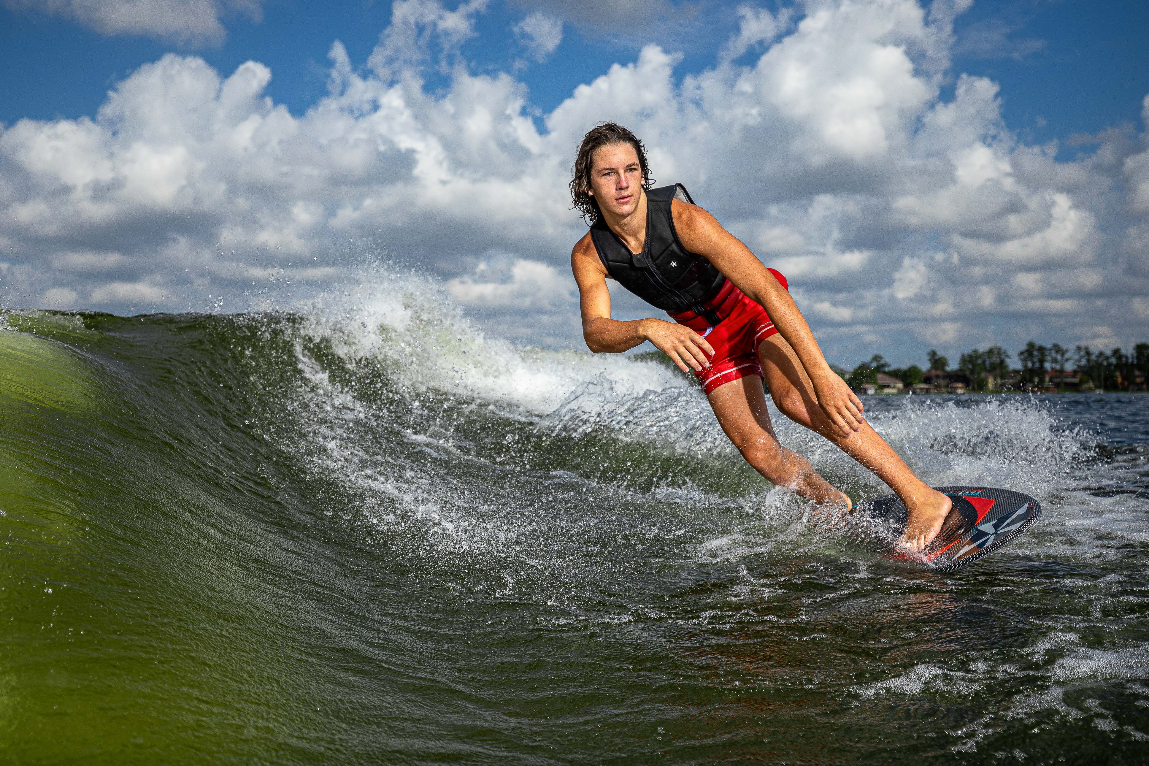 A young man rides a wave on a 2025 Phase 5 Key Jett Shreds skim board, showcasing skill and balance on water.