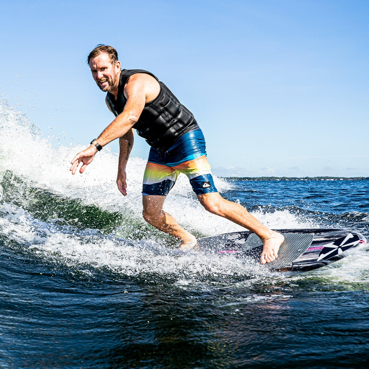 Man riding the 2025 Phase 5 Oogle Skim Board on water, showcasing action and excitement in a sunny outdoor setting.