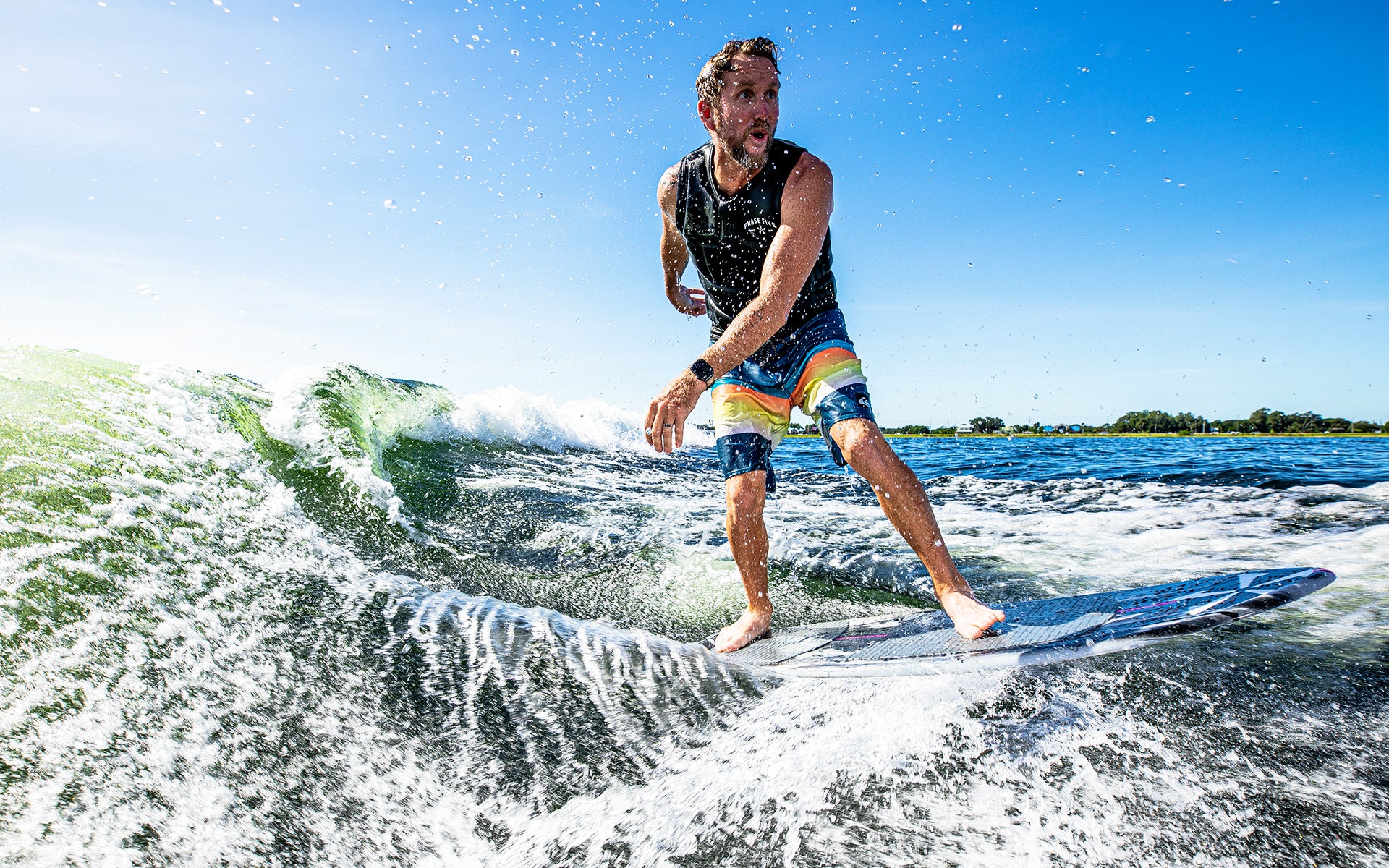 A person riding the 2025 Phase 5 Oogle Skim Board on a wave, showcasing its performance and design in action.