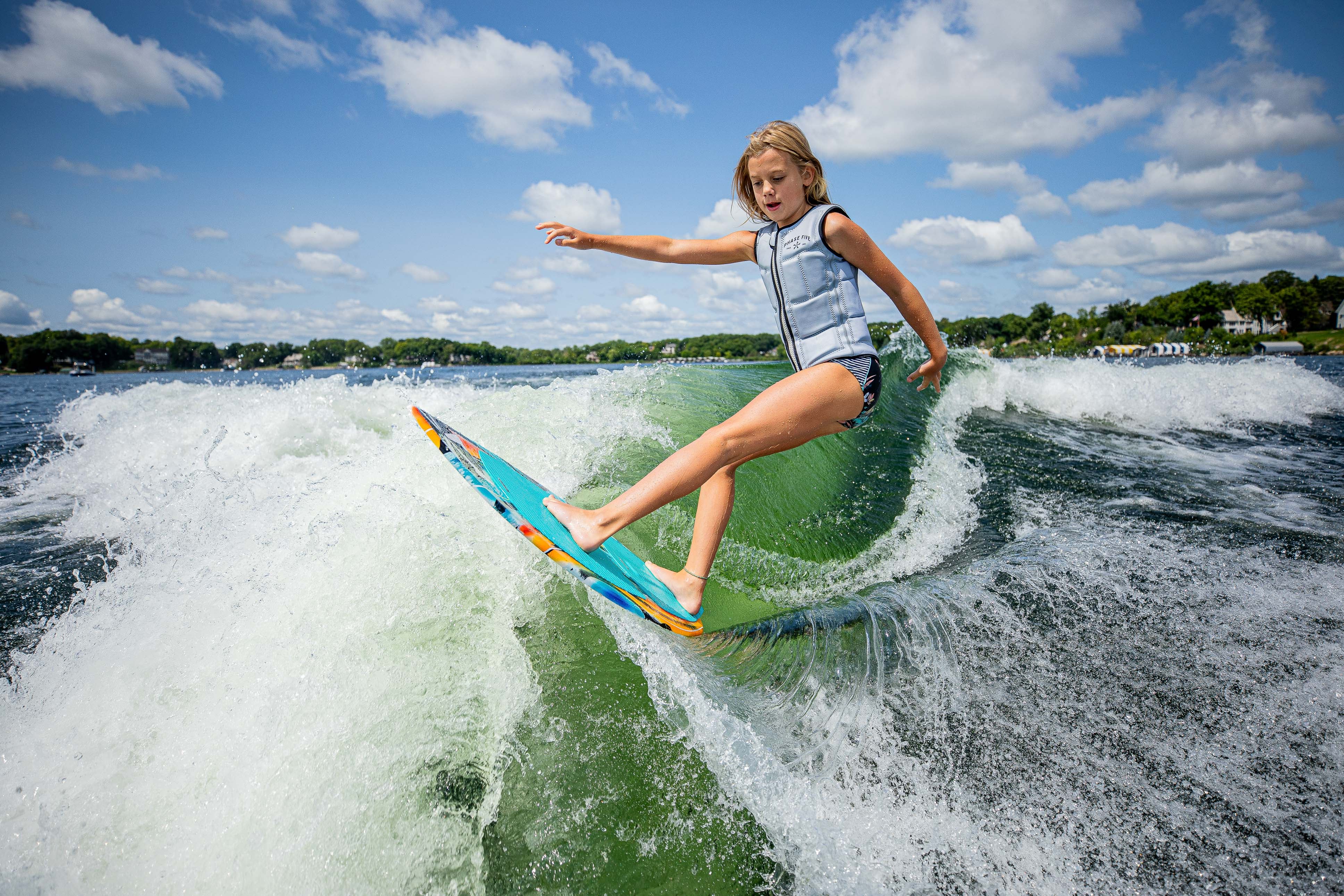 A child rides the 2025 Phase 5 Scamp Skim Board on a wave, showcasing skill and excitement on the water.