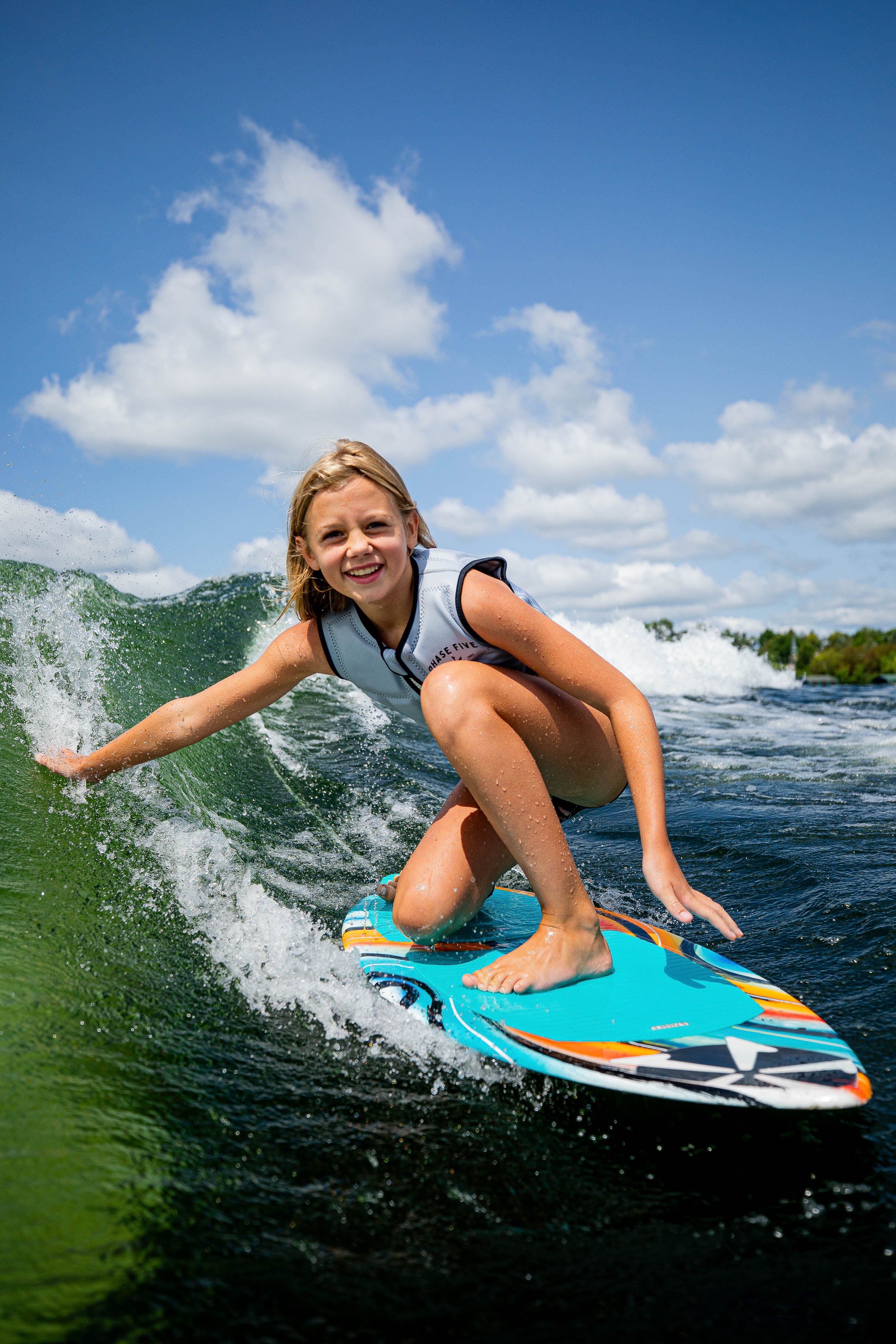 A young girl rides a wave on a 2025 Phase 5 Scamp skim board, showcasing her skills and enjoying the water.
