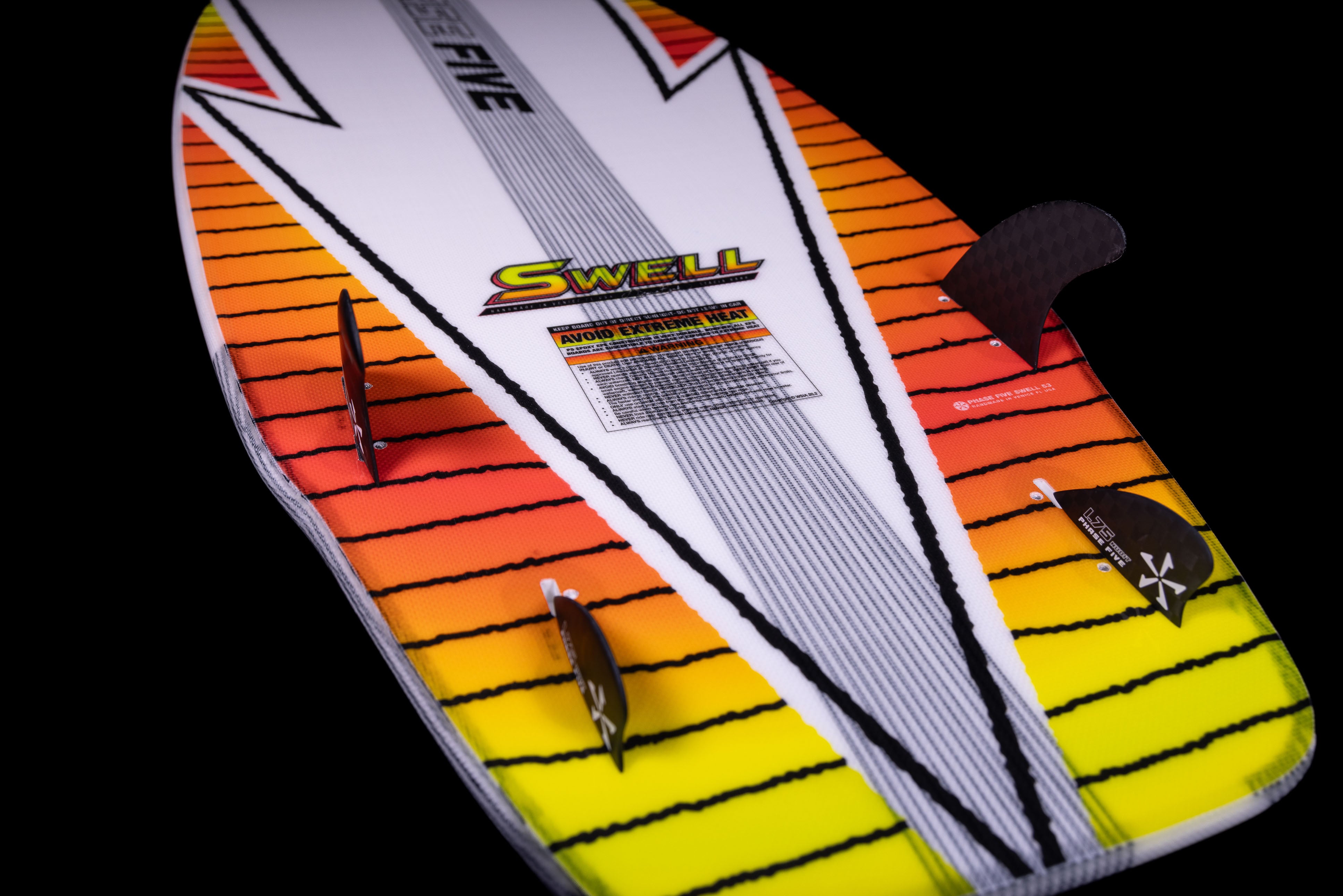 Colorful 2025 Phase 5 Swell surfboard with orange, yellow, and white design, featuring fins, a textured deck, and warning labels.