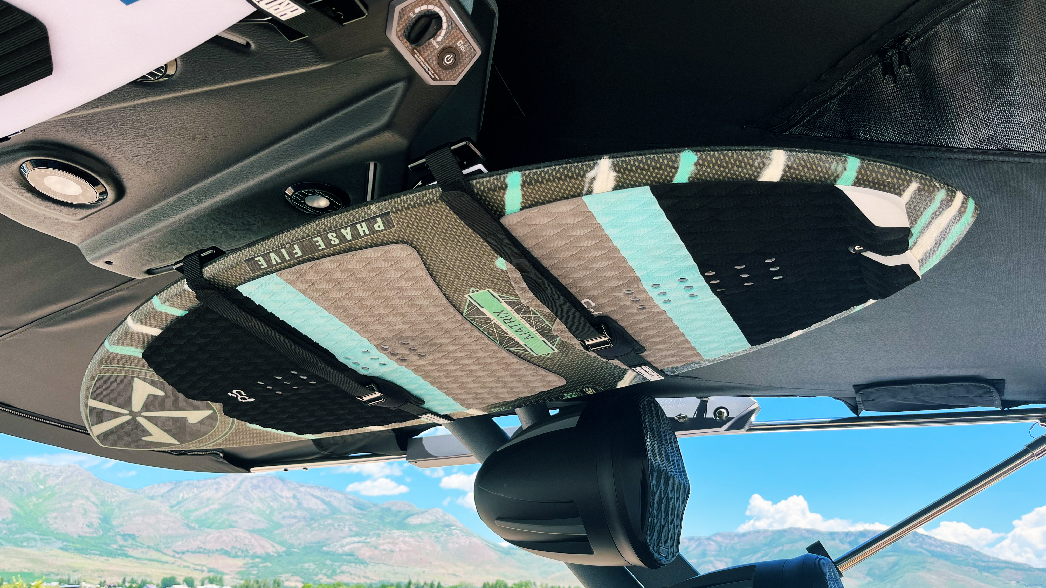 Surfboard secured on GX Towers XR1 Surf Rack inside a vehicle, with scenic mountains and blue sky in the background.