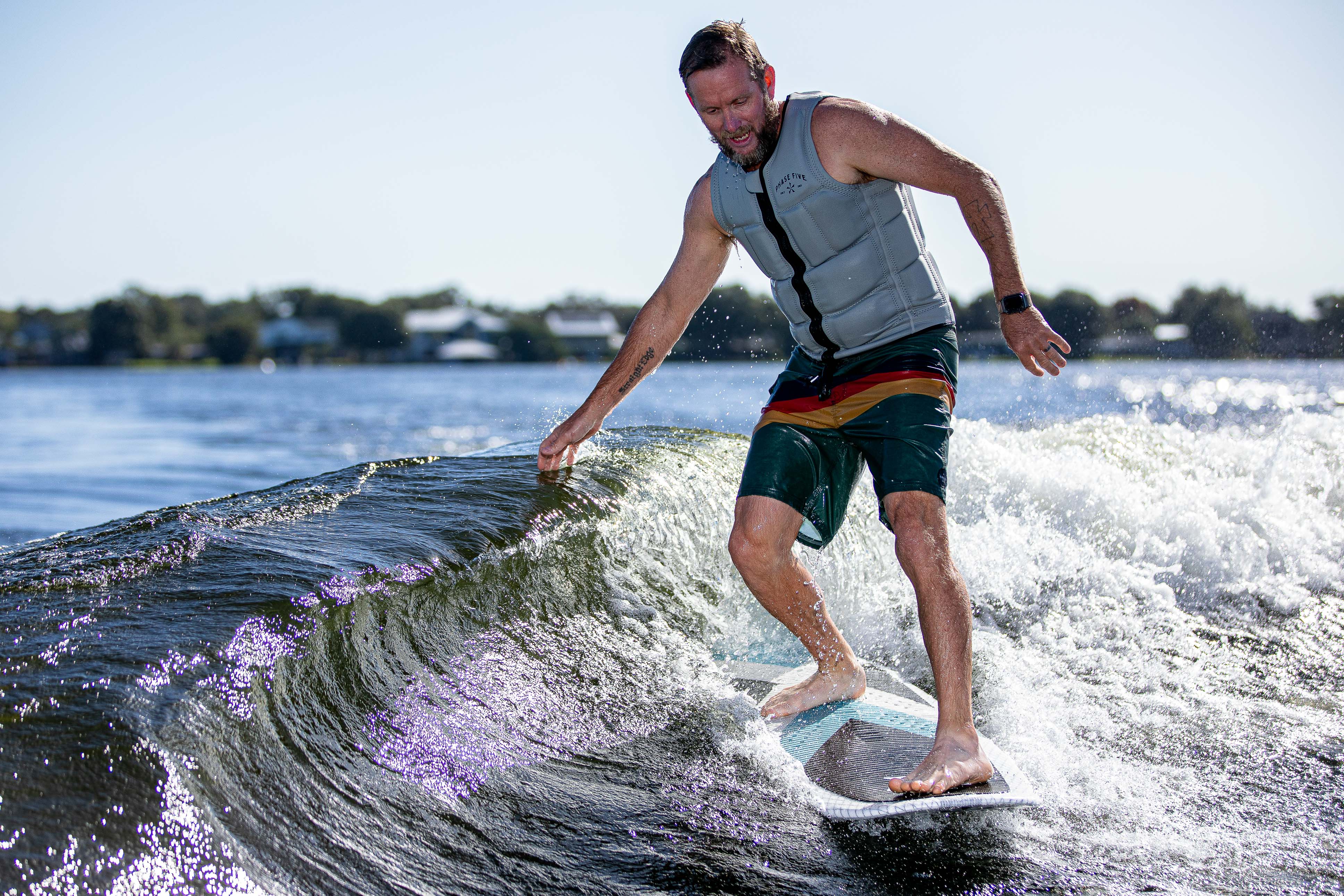 Man riding the waves on the 2025 Phase 5 Zeevo Surf Board, wearing a life vest and colorful shorts, surfing on a sunny day.