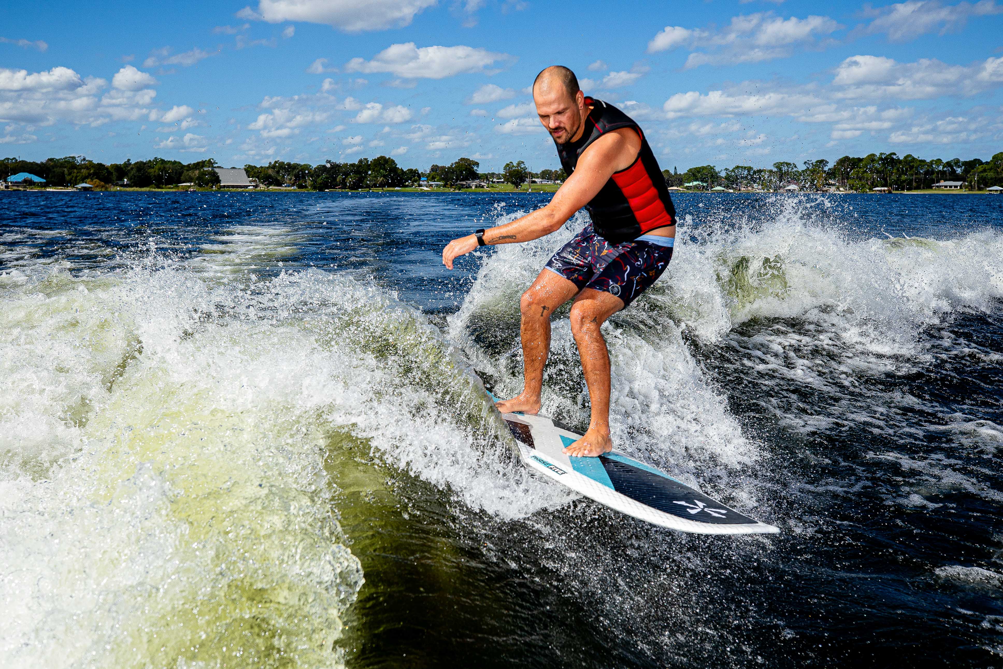 Man surfing on the 2025 Phase 5 Zeevo Surf Board on a lake with blue skies and white clouds.