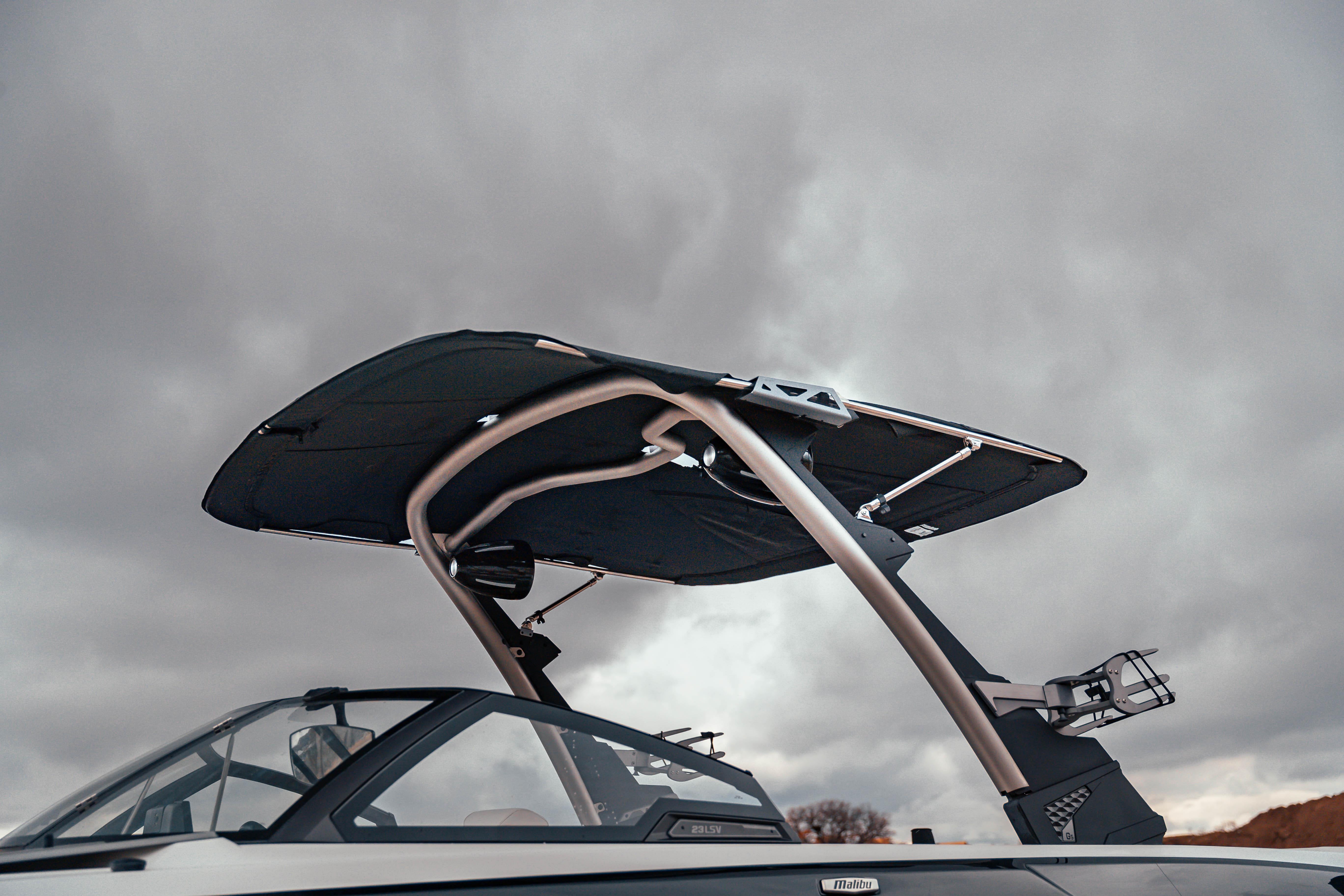 Malibu VTX boat with a black bimini top and ski tower, set against a cloudy sky.
