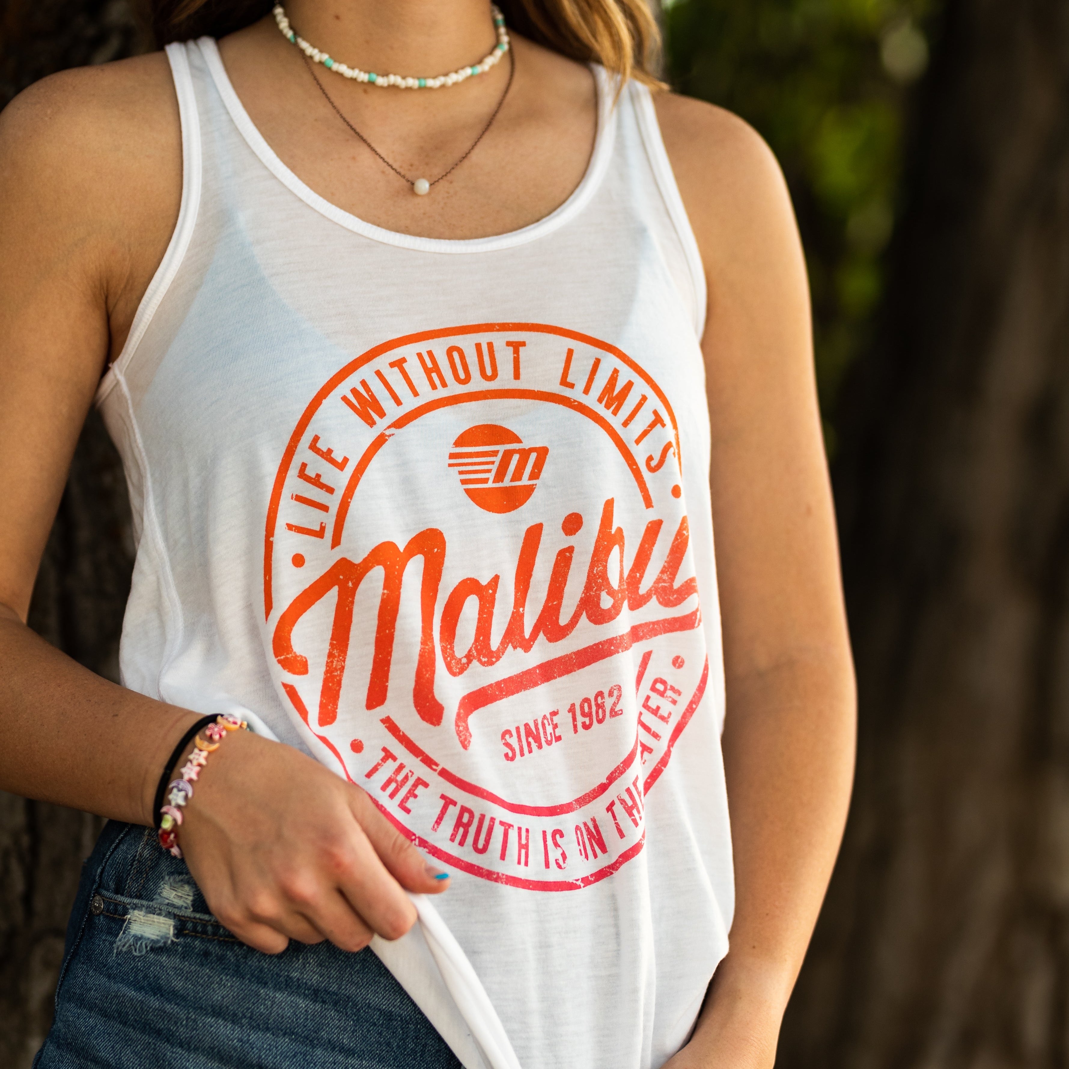 Women's white tank top with orange Malibu logo and text, featuring a sleeveless design and relaxed fit.