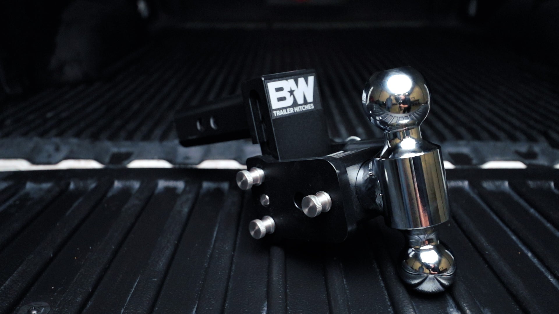 Black B&W TOW & STOW adjustable ball mount with chrome hitch ball, mounted on a black surface.