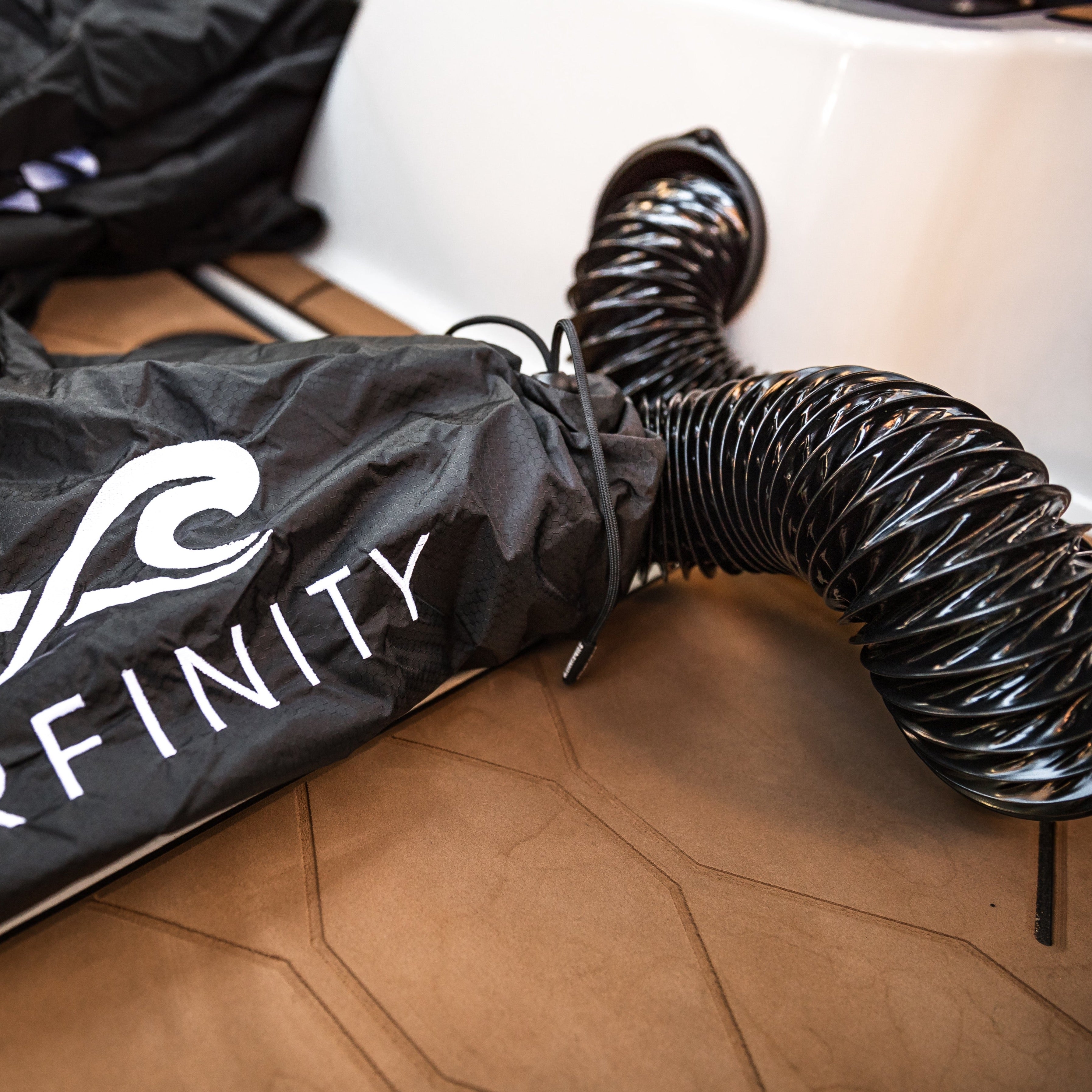 Heated boat blanket by Surfinity with a black, flexible hose, partially inside a black carrying bag, on a wooden surface.