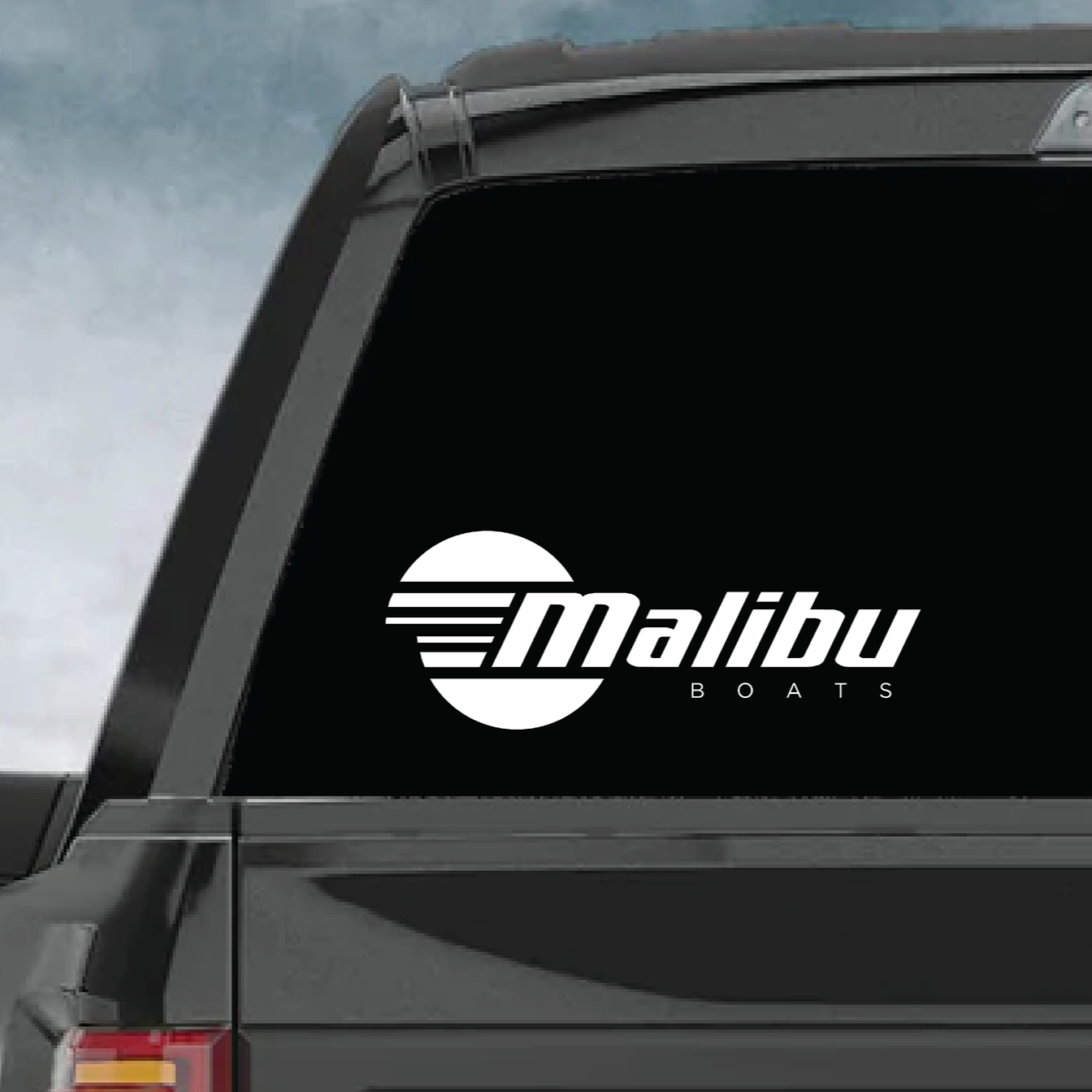 Alt text: "12-inch Malibu Boats die cut decal on the rear window of a truck, displaying the brand's logo in white against the tinted glass."