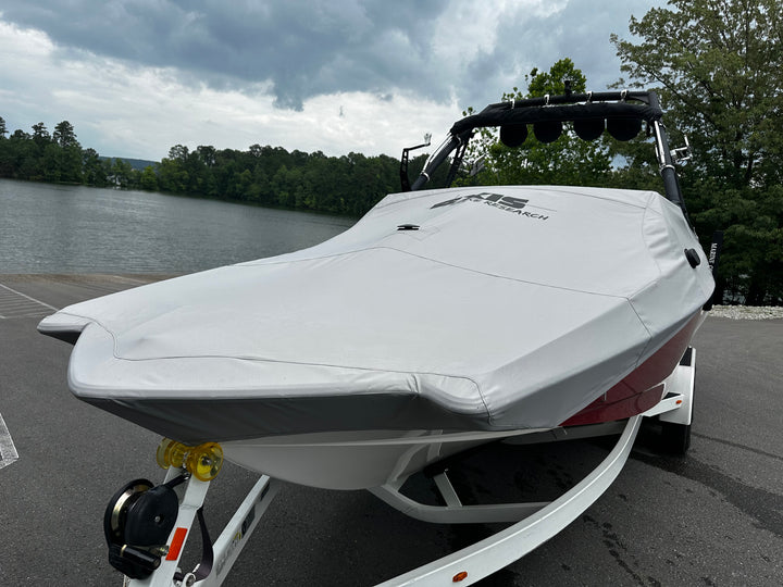 White A24 cover on a boat trailer, parked near a lake with trees and cloudy sky in the background.