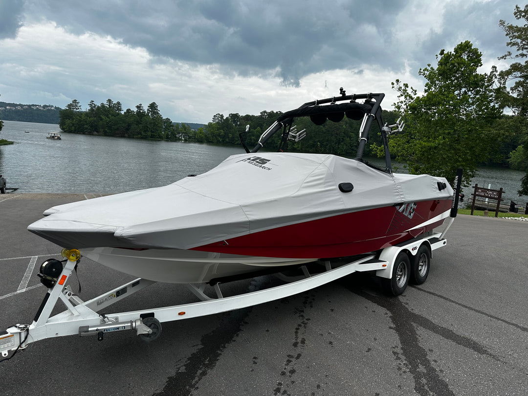 A white and red FatAX Tower boat on a trailer near a lake with trees and cloudy sky in the background.