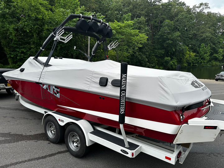 A red and white A24 boat on a trailer, covered with a gray protective cover, parked outdoors near trees and water.