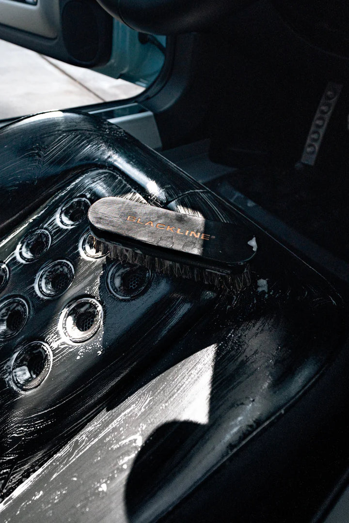 Leather brush resting on a cleaned leather seat, showcasing its bristles and sleek design for effective maintenance.