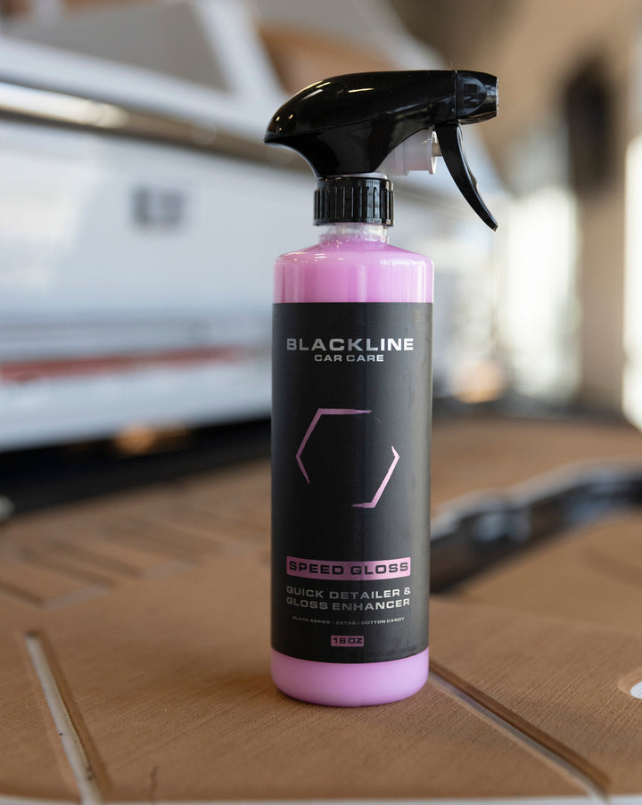 Blackline Speed Gloss Quick Detailer spray bottle for car care, featuring a black and pink label, on a wooden surface.