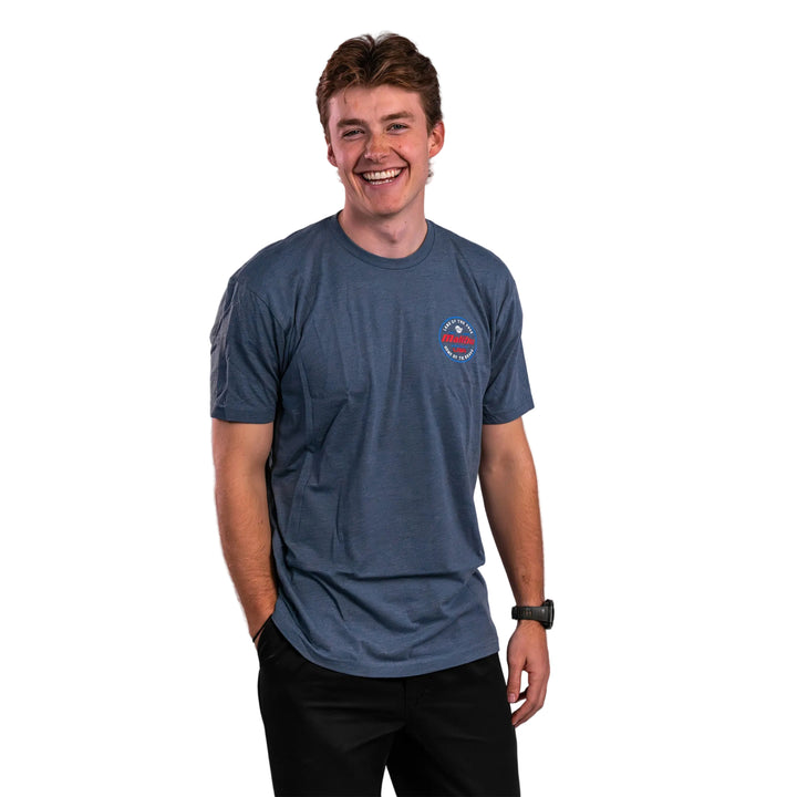 A young man wearing a blue Malibu Brave Tee, smiling confidently with hands in pockets, showcasing a casual style.