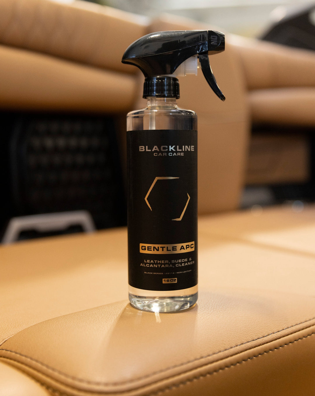 Blackline Gentle APC leather, suede, and Alcantara cleaner in a clear spray bottle with black label, placed on a beige car seat.