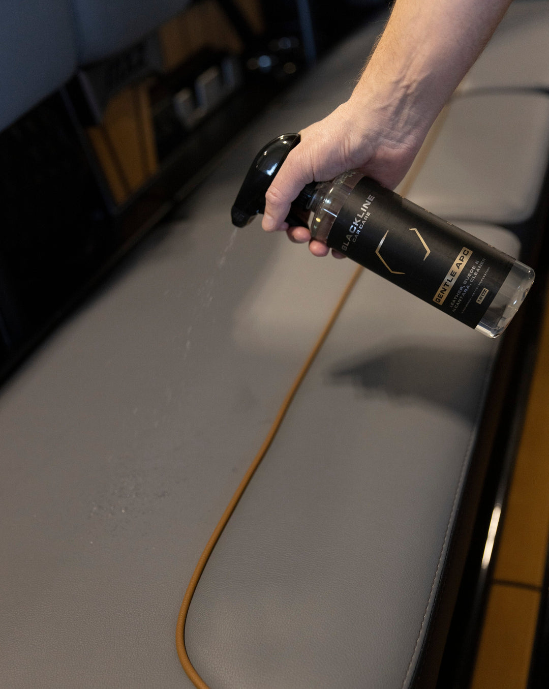 Hand spraying Blackline Gentle APC cleaner on a surface, demonstrating its gentle cleaning for delicate materials.