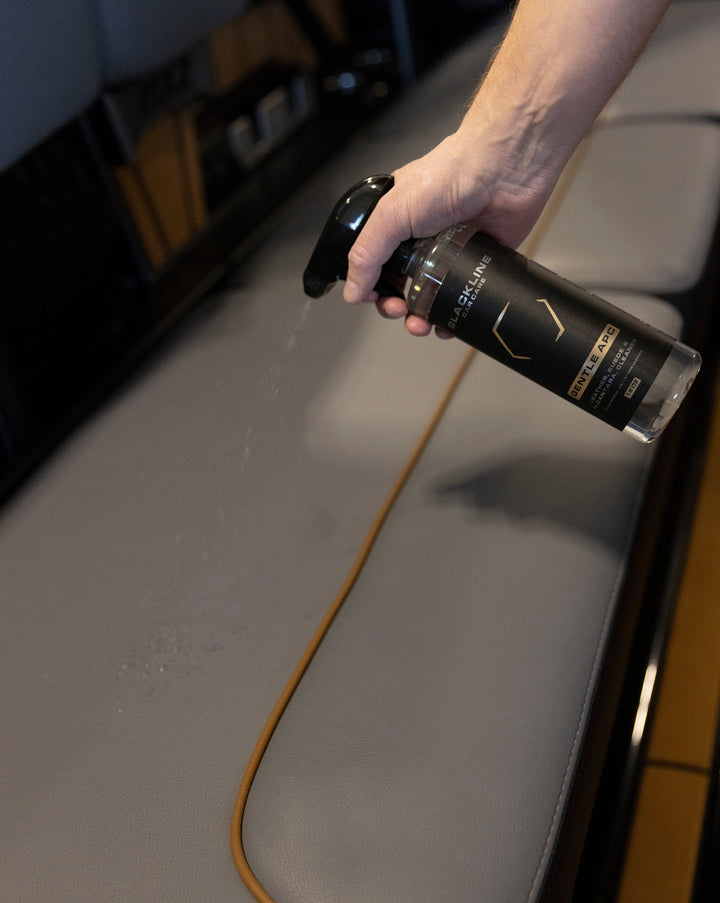 Hand spraying Blackline Gentle APC cleaner on a surface, demonstrating its gentle cleaning for delicate materials.