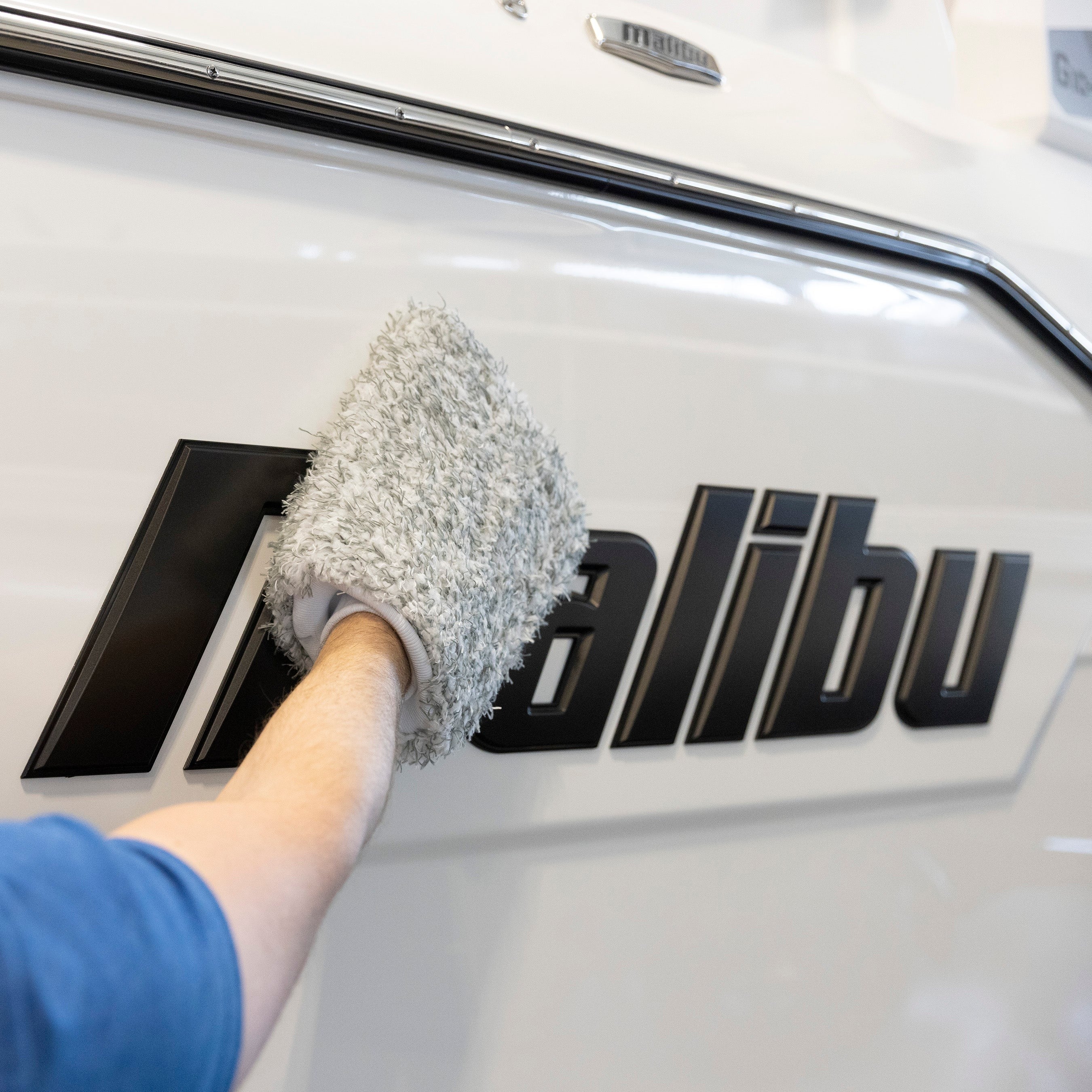 A person cleaning a car's logo with a gray microfiber wash mitt, designed for gentle, effective vehicle washing.