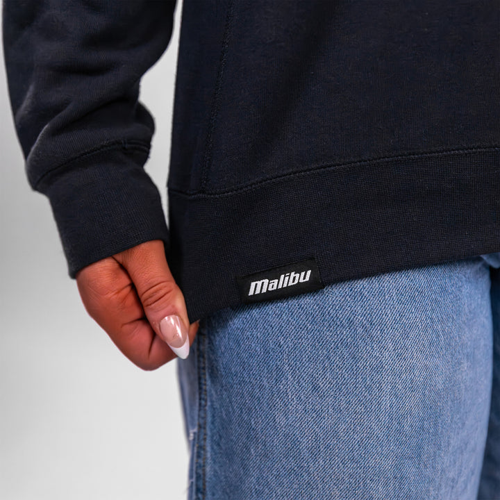 Malibu Varsity Crewneck featuring a close-up of the brand label on the hem, styled with denim jeans.
