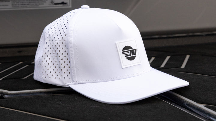 White Malibu Swell hat with perforated sides, a curved brim, and a black and white logo patch on the front.