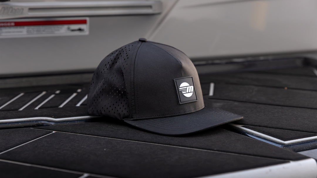Black Malibu Swell Hat with a perforated crown and a rectangular logo patch on the front, placed on a dark surface.