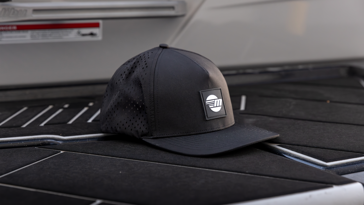 Black Malibu Swell Hat with a perforated crown and a rectangular logo patch on the front, placed on a dark surface.