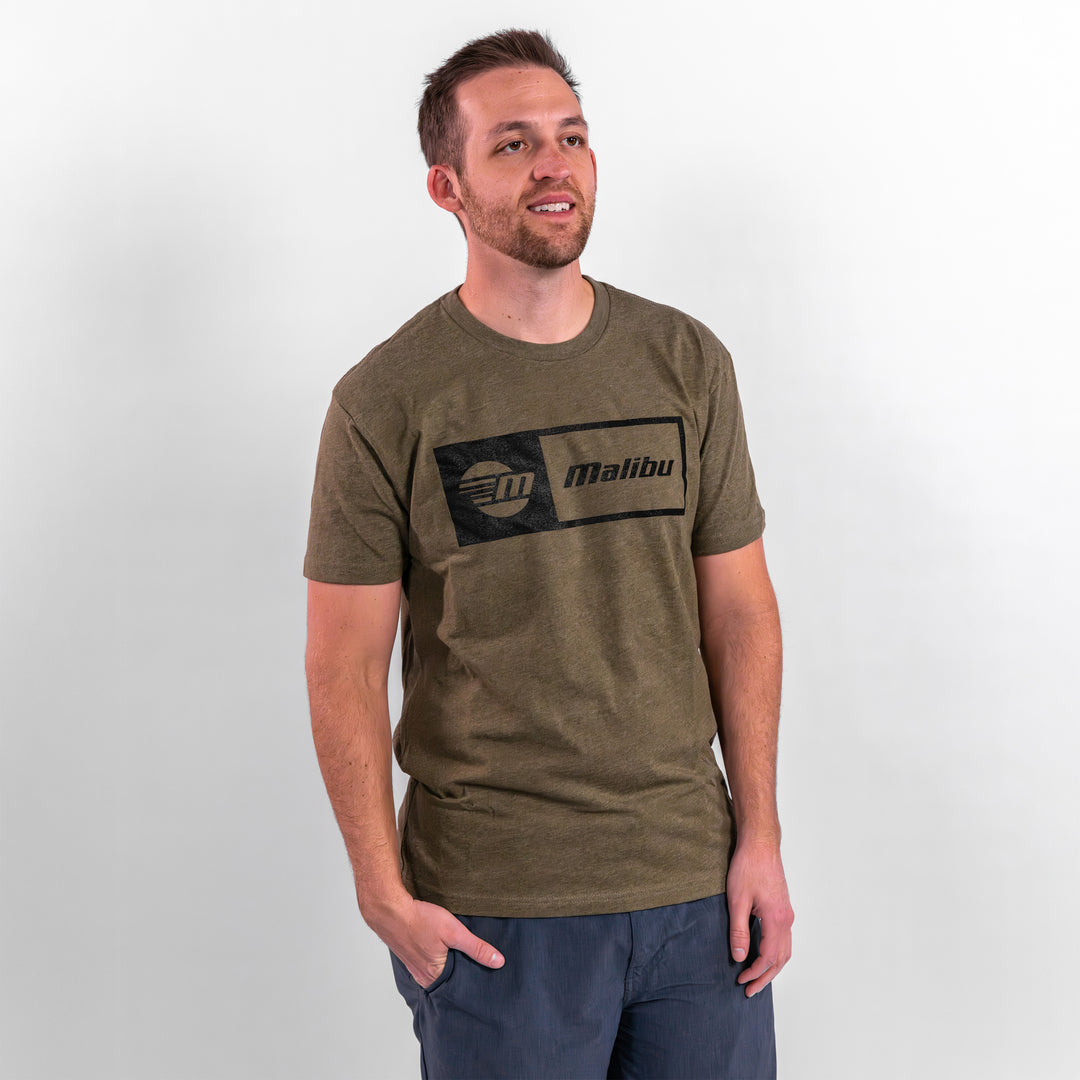 Man wearing a Malibu Statement Tee in olive green, featuring a black logo design, standing against a neutral background.