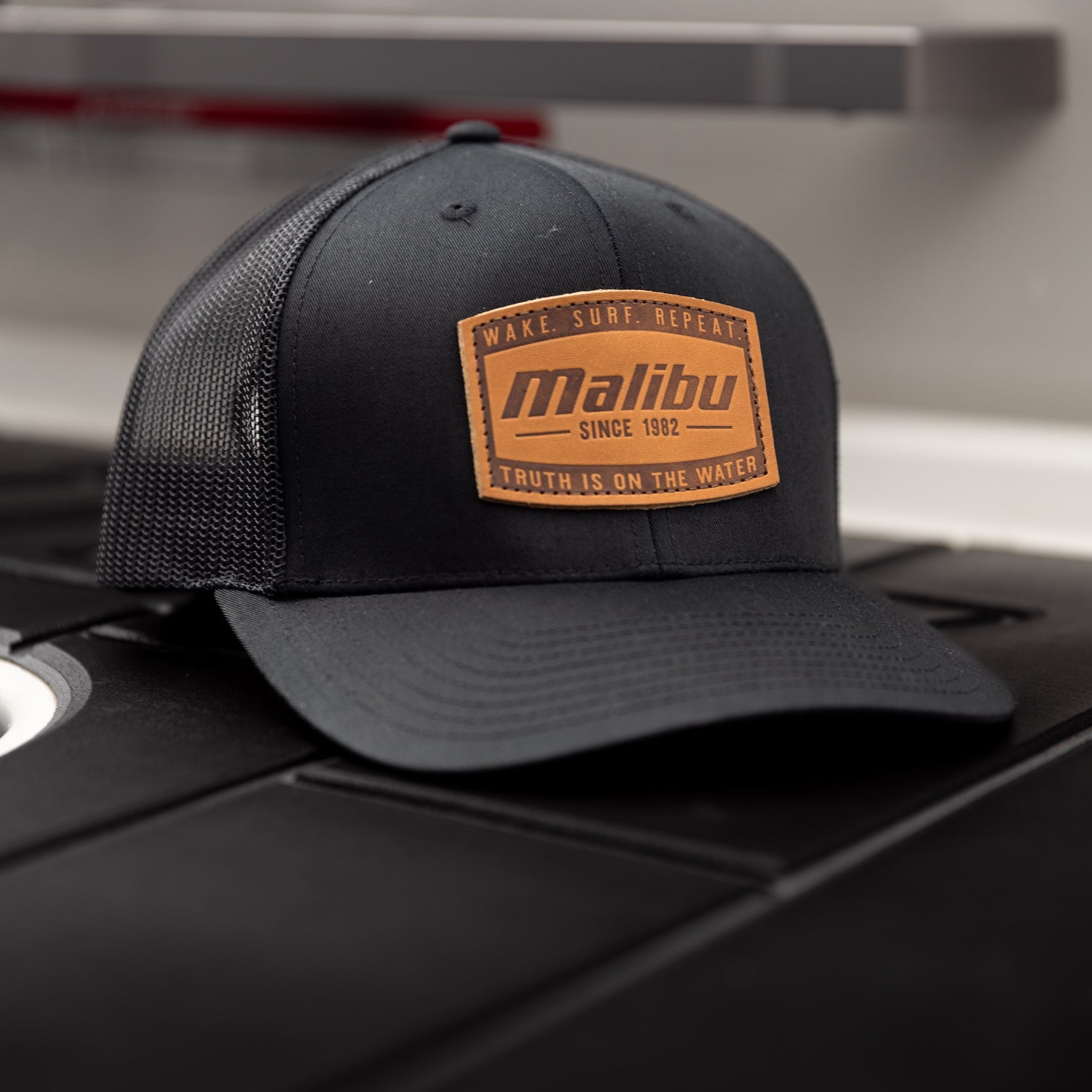 Black trucker-style ranger hat with a brown patch reading "Malibu Since 1982" and slogans about surfing and water.
