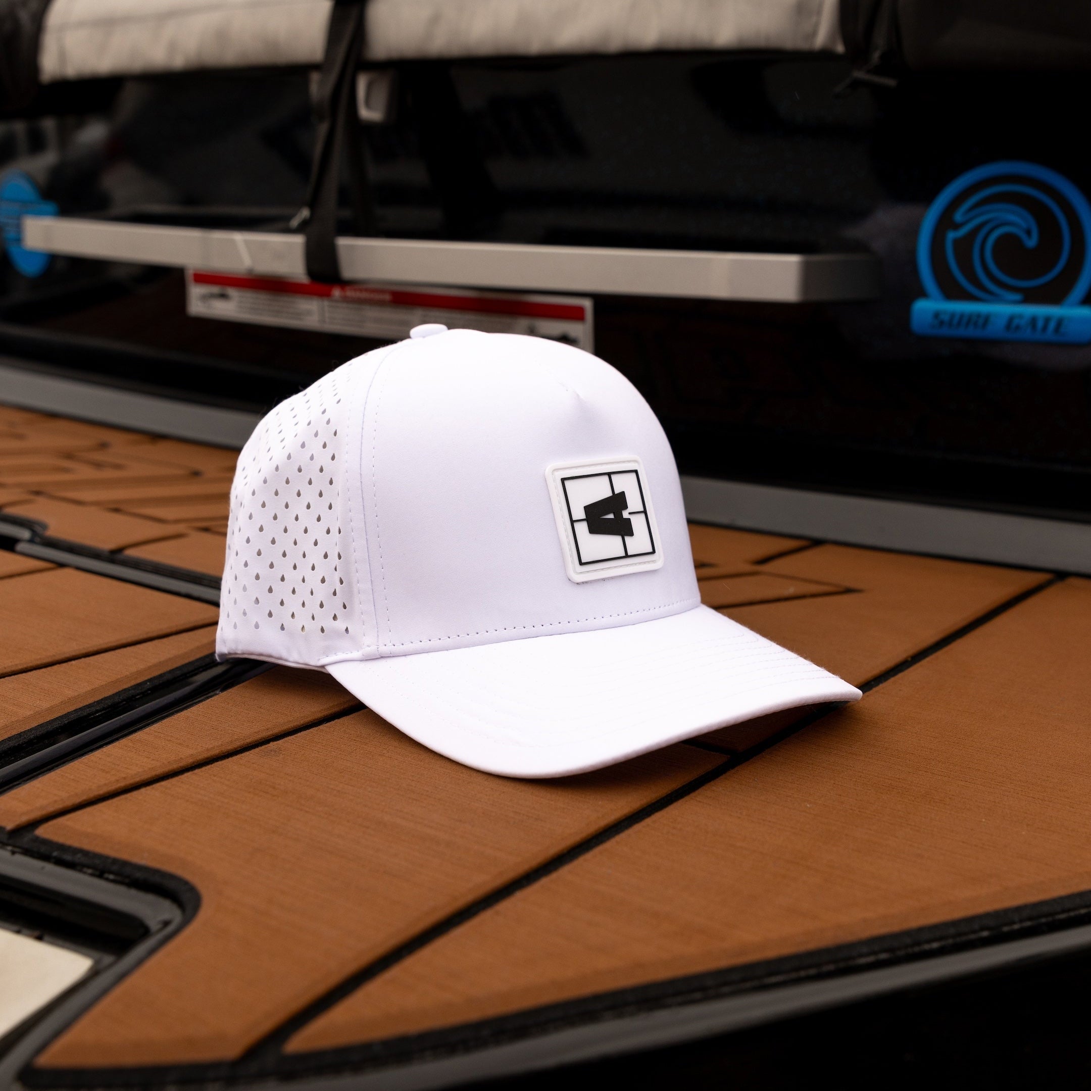 White Axis Swell Hat with mesh panels and logo patch, placed on a boat deck near a wakeboard.