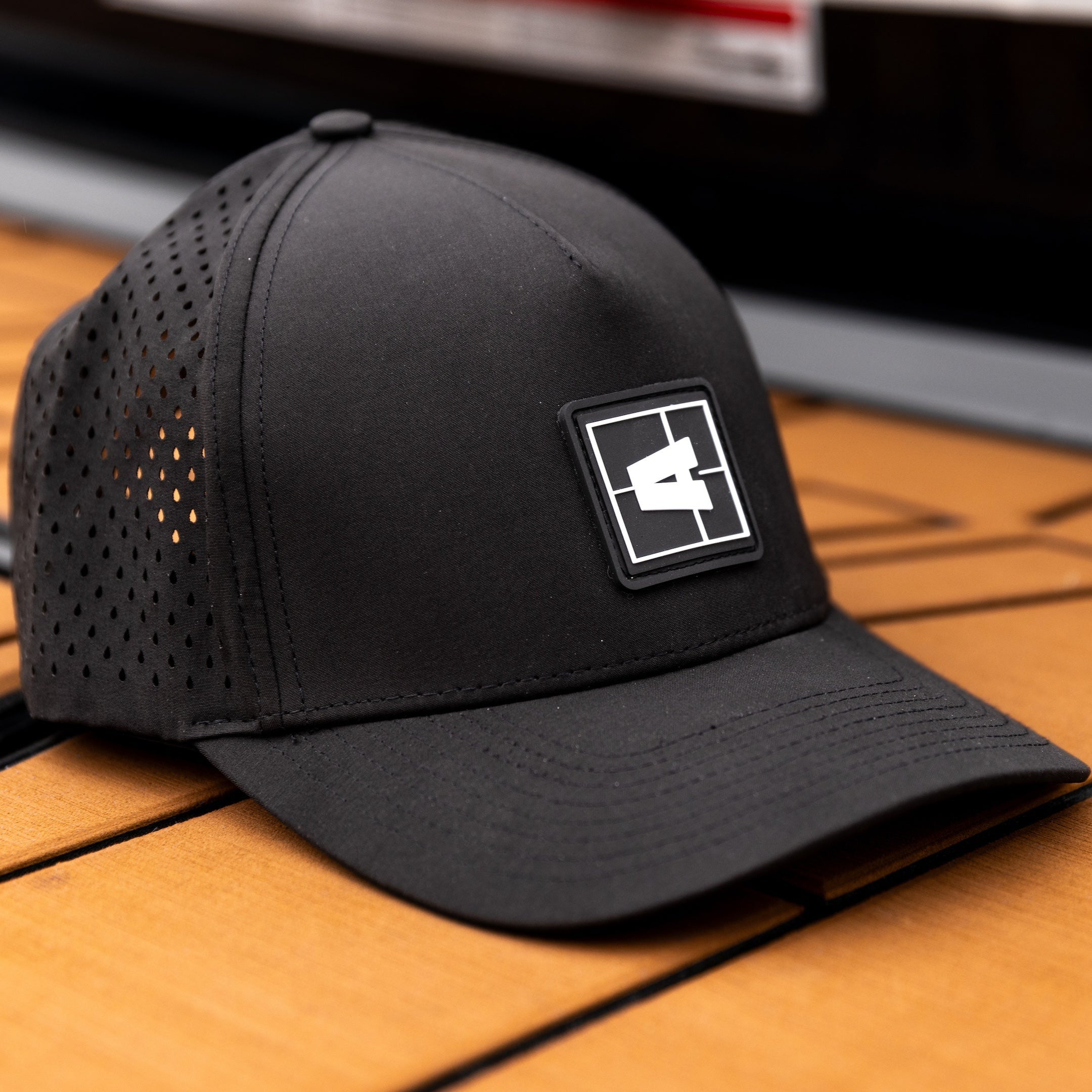 Black Axis Swell Hat with perforated panels and a rectangular logo patch on the front, placed on a wooden surface.